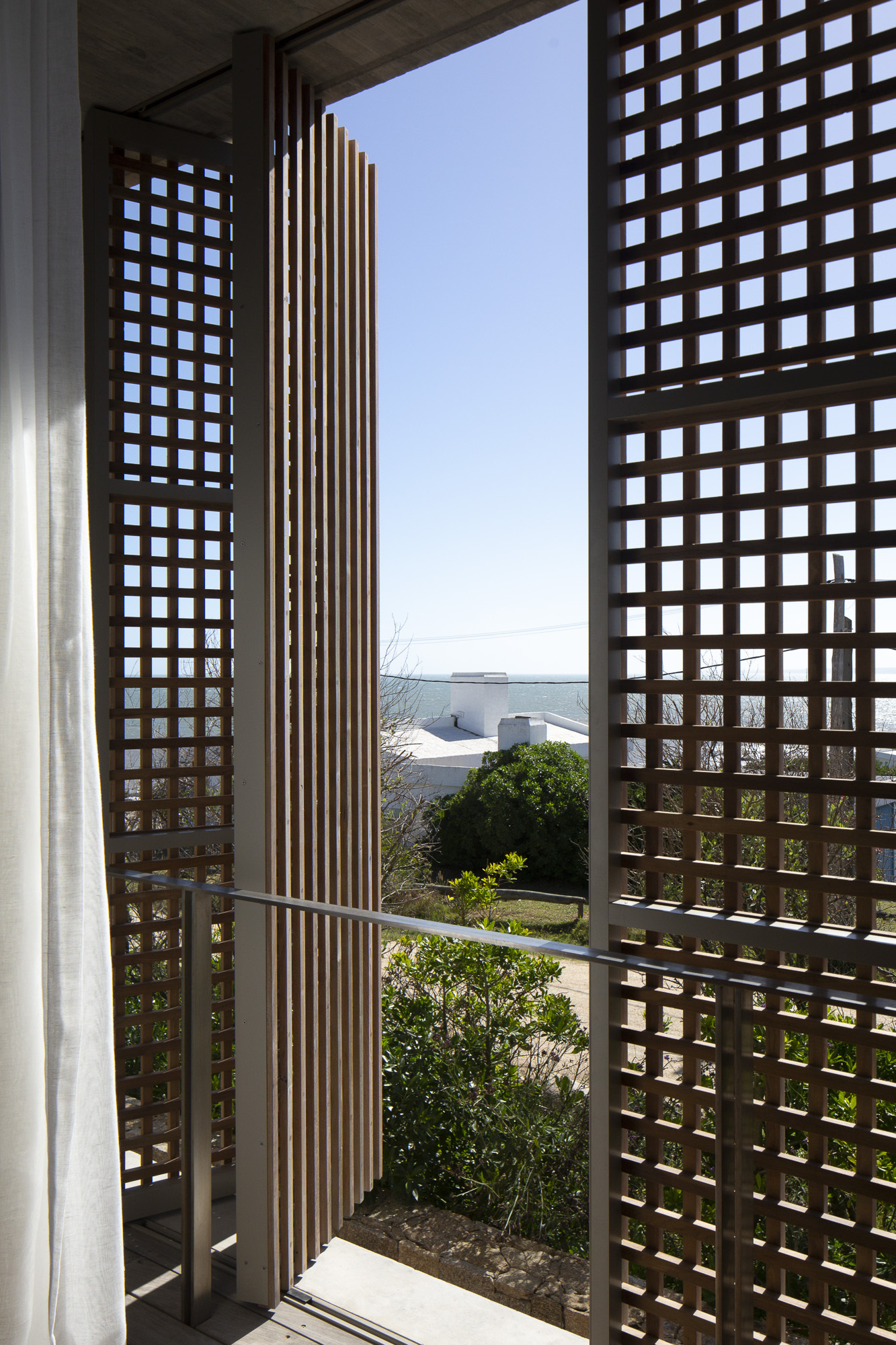 Interior view through the lattice screen opening to a planted courtyard with ocean beyond