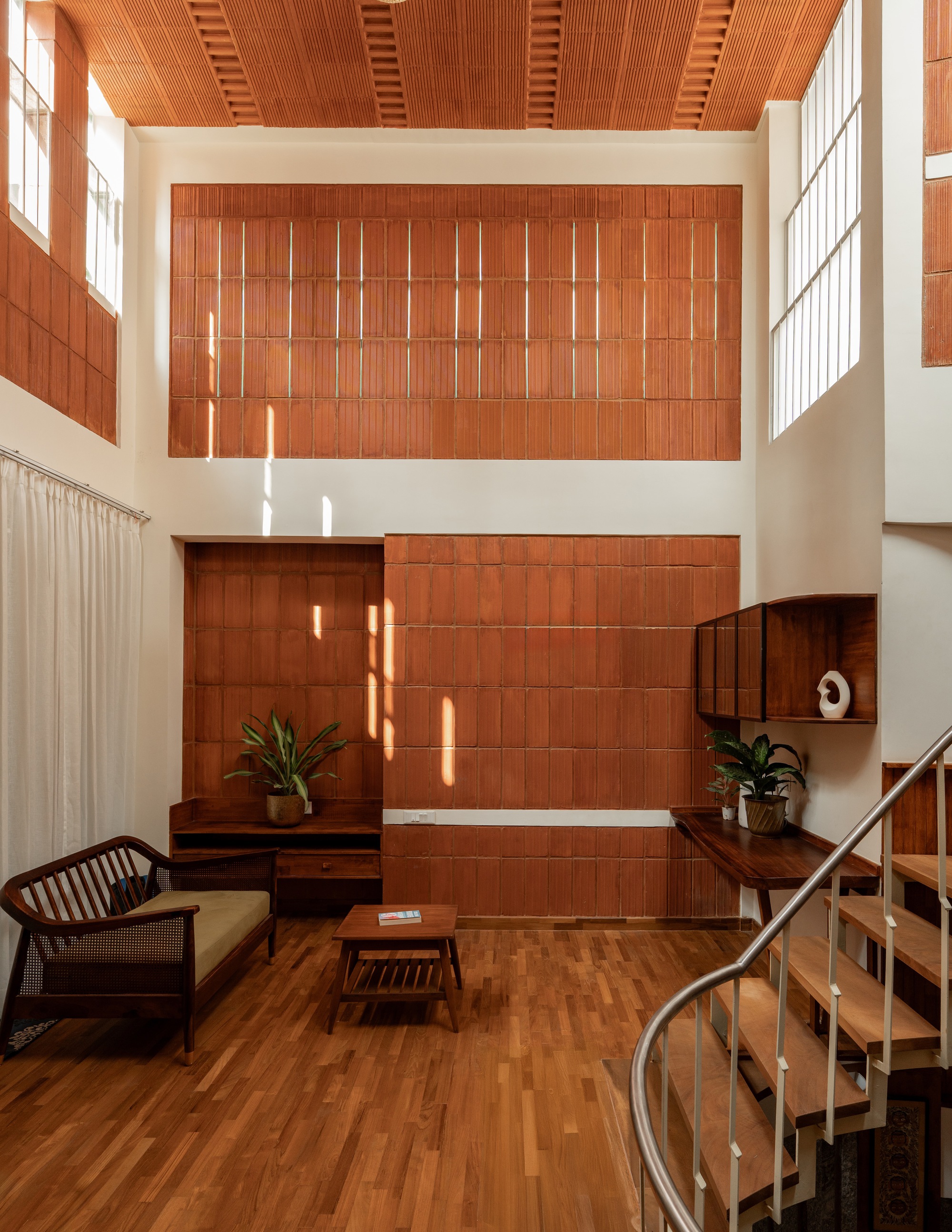 Double-height living room with terracotta tile wall and slatted timber ceiling in afternoon sun