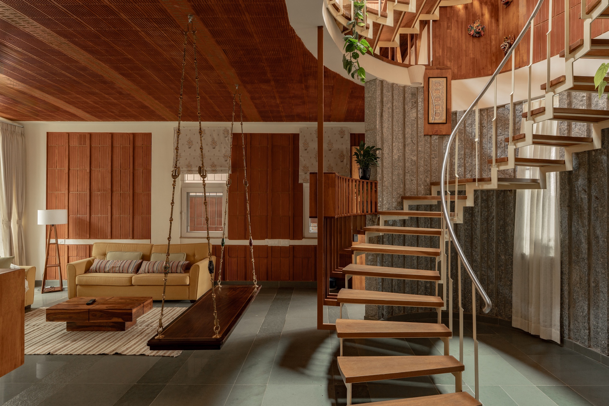 Living area with suspended wood swing bench and spiral stair under a timber-clad vaulted ceiling