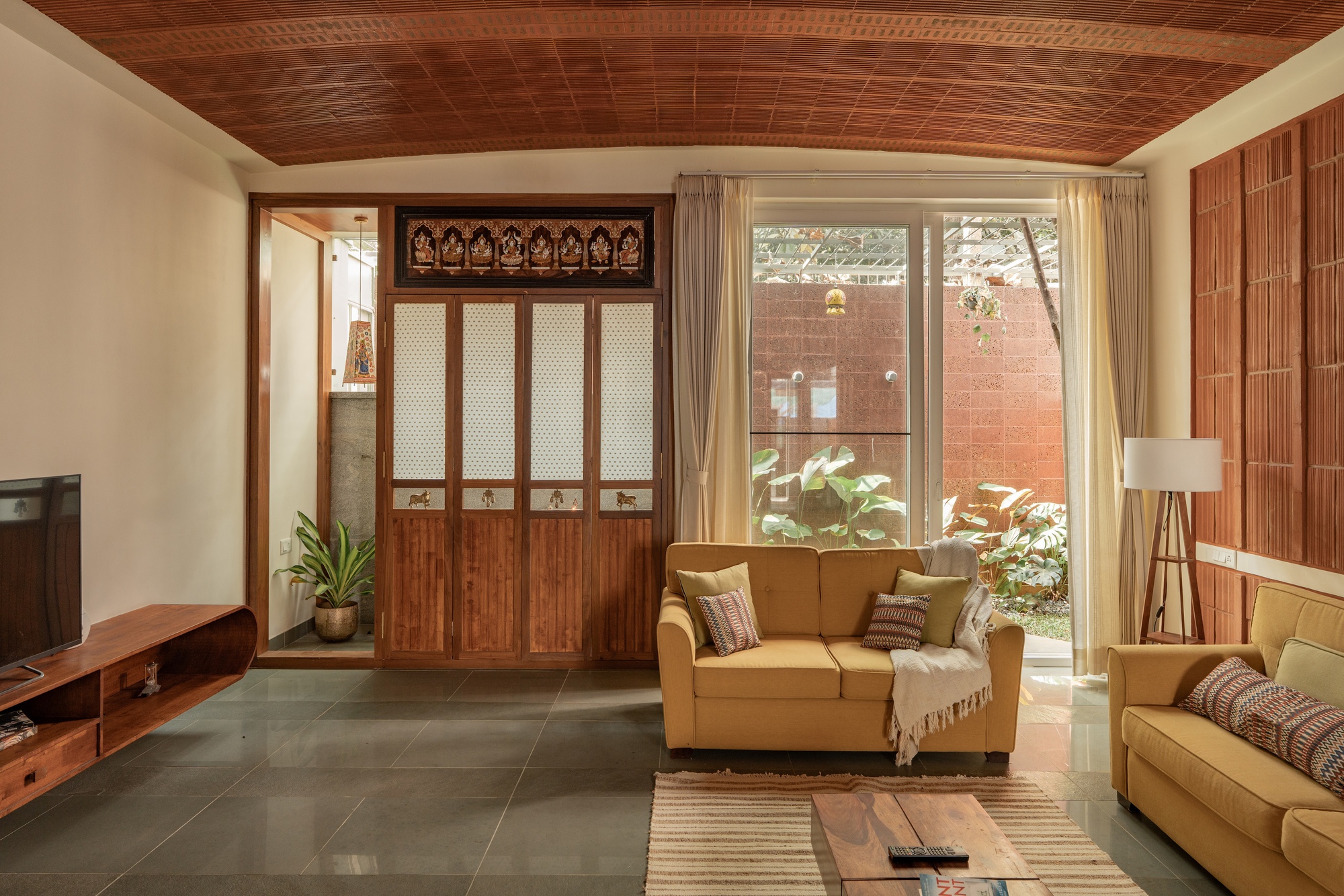 Living room with timber screen doors, slatted wood ceiling and courtyard view through glazed doors