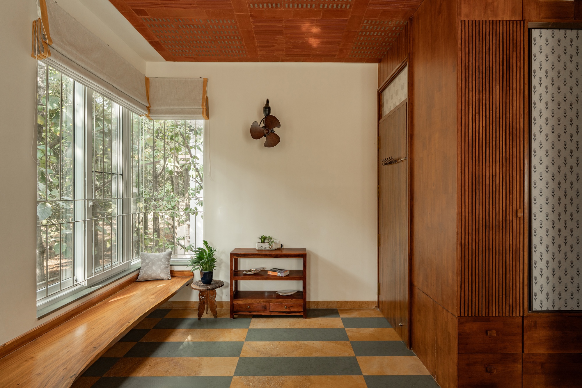 Entrance nook with built-in timber bench, checkered floor tiles and garden view through tall windows