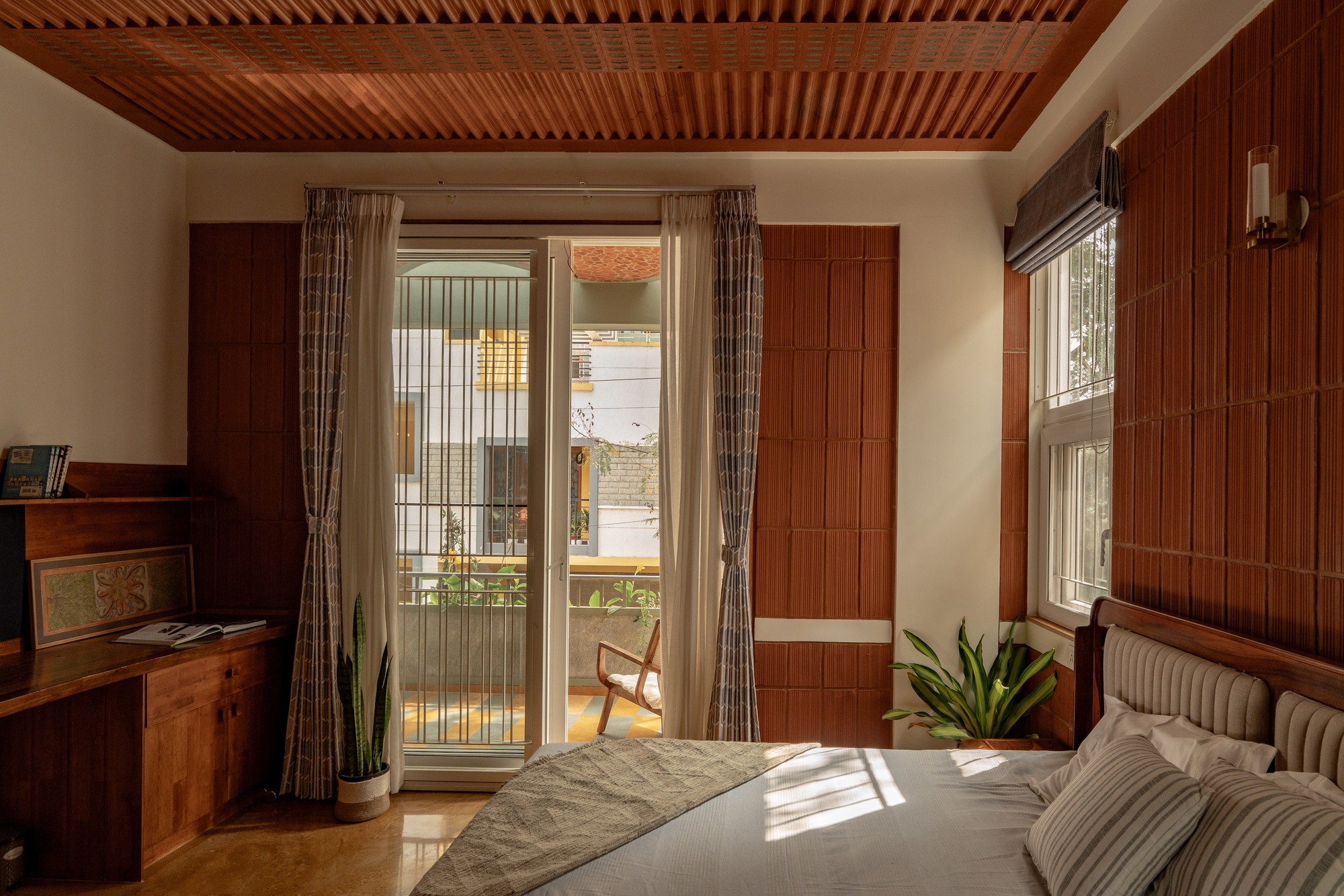 Bedroom with slatted timber ceiling and walls opening to a balcony with afternoon sun