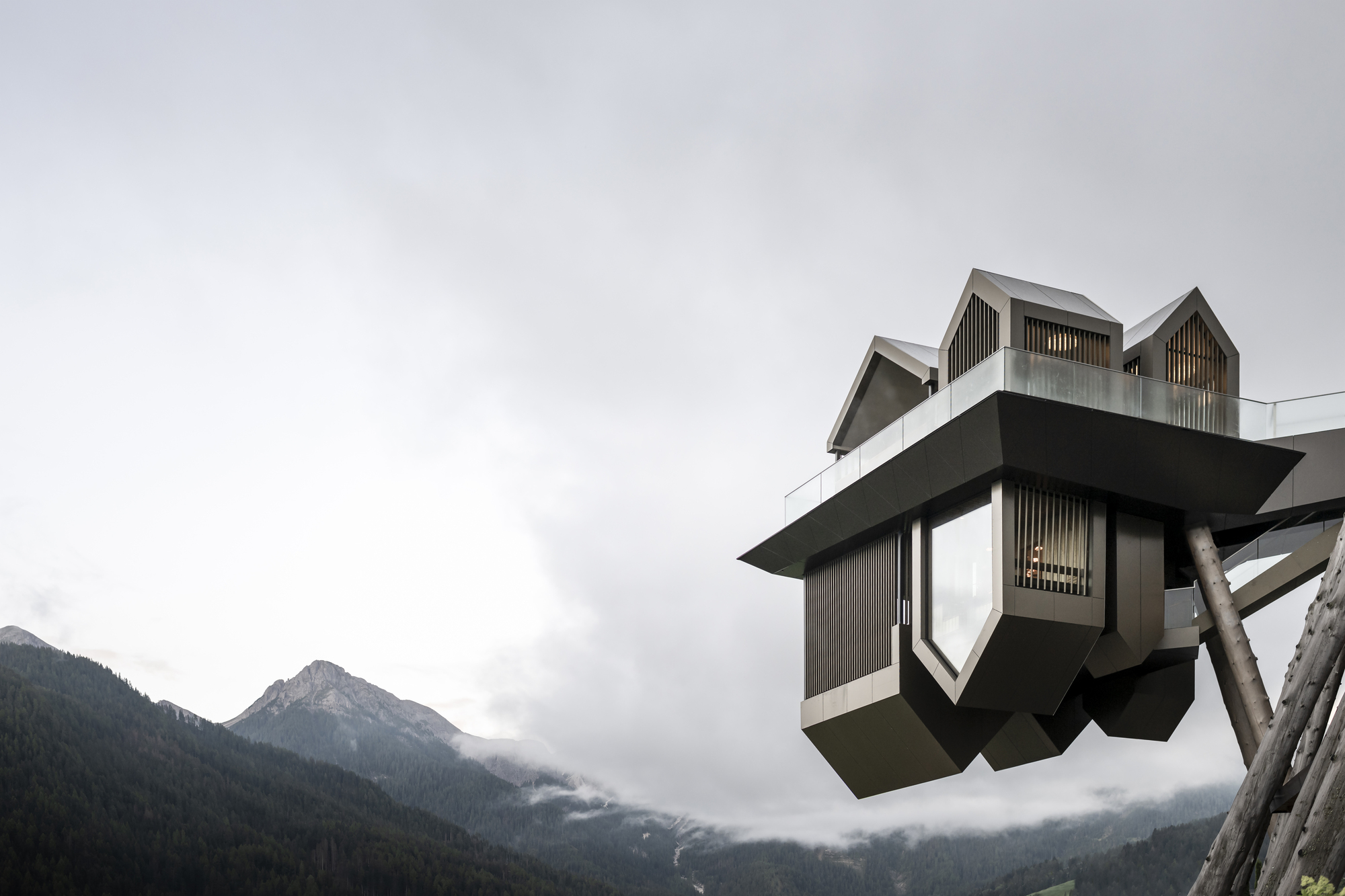 Cantilevered viewing platform with faceted metal panels set against fog-shrouded mountain peaks