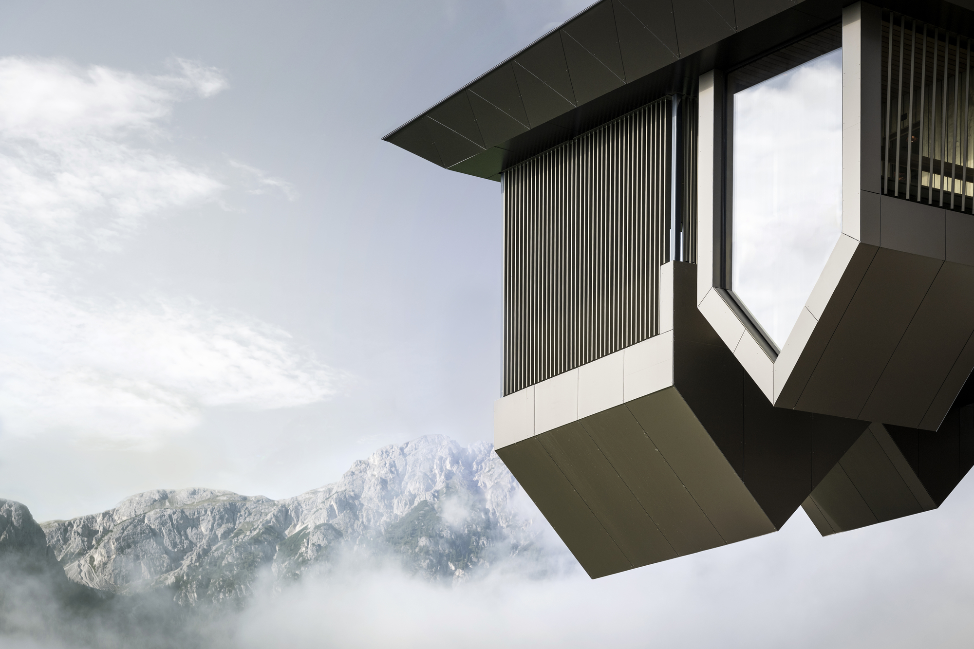 Corner detail of the faceted volume with vertical metal slats floating above misty alpine ridges