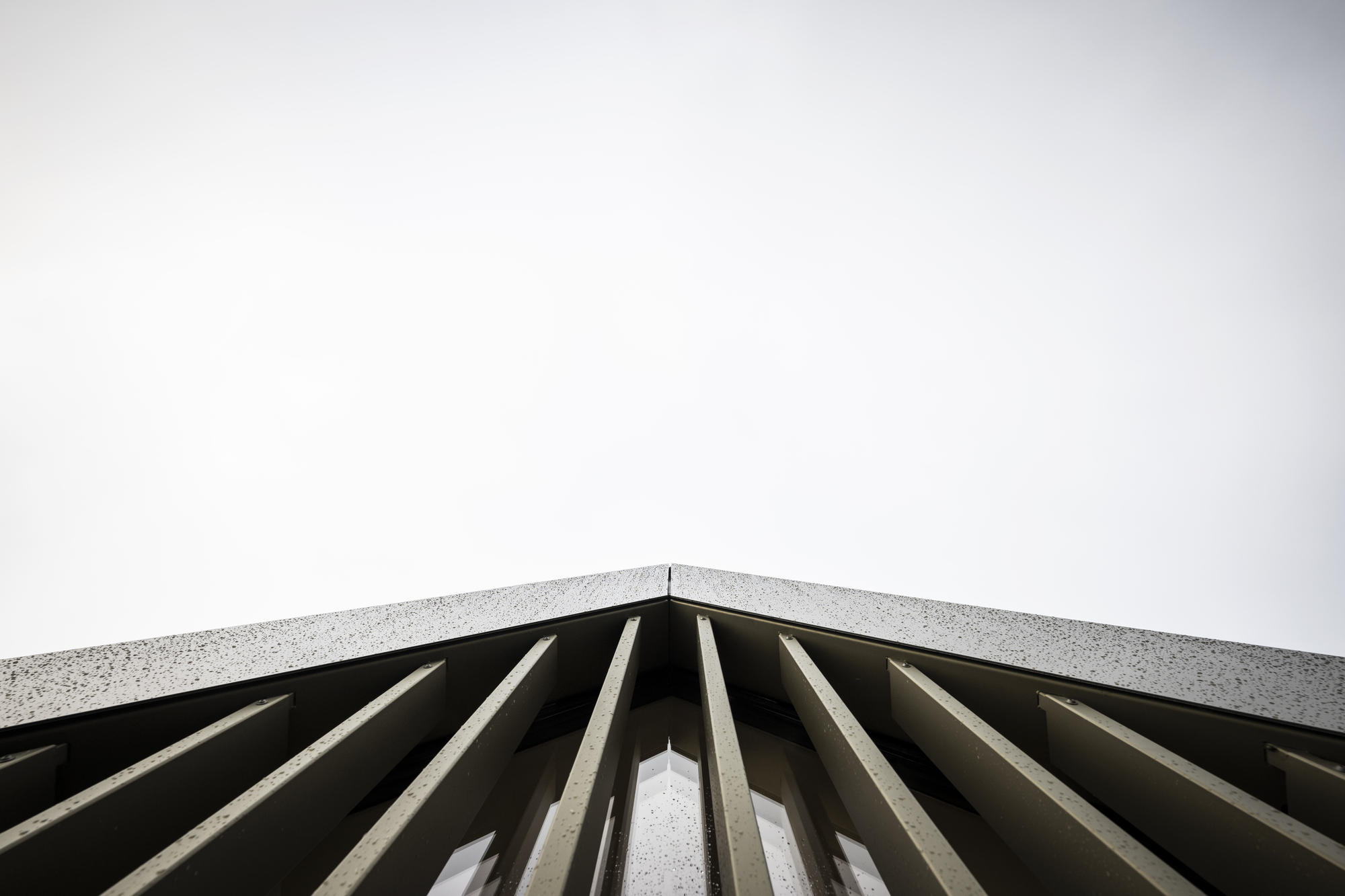 Upward view of vertical concrete fins meeting aggregate coping under pale sky
