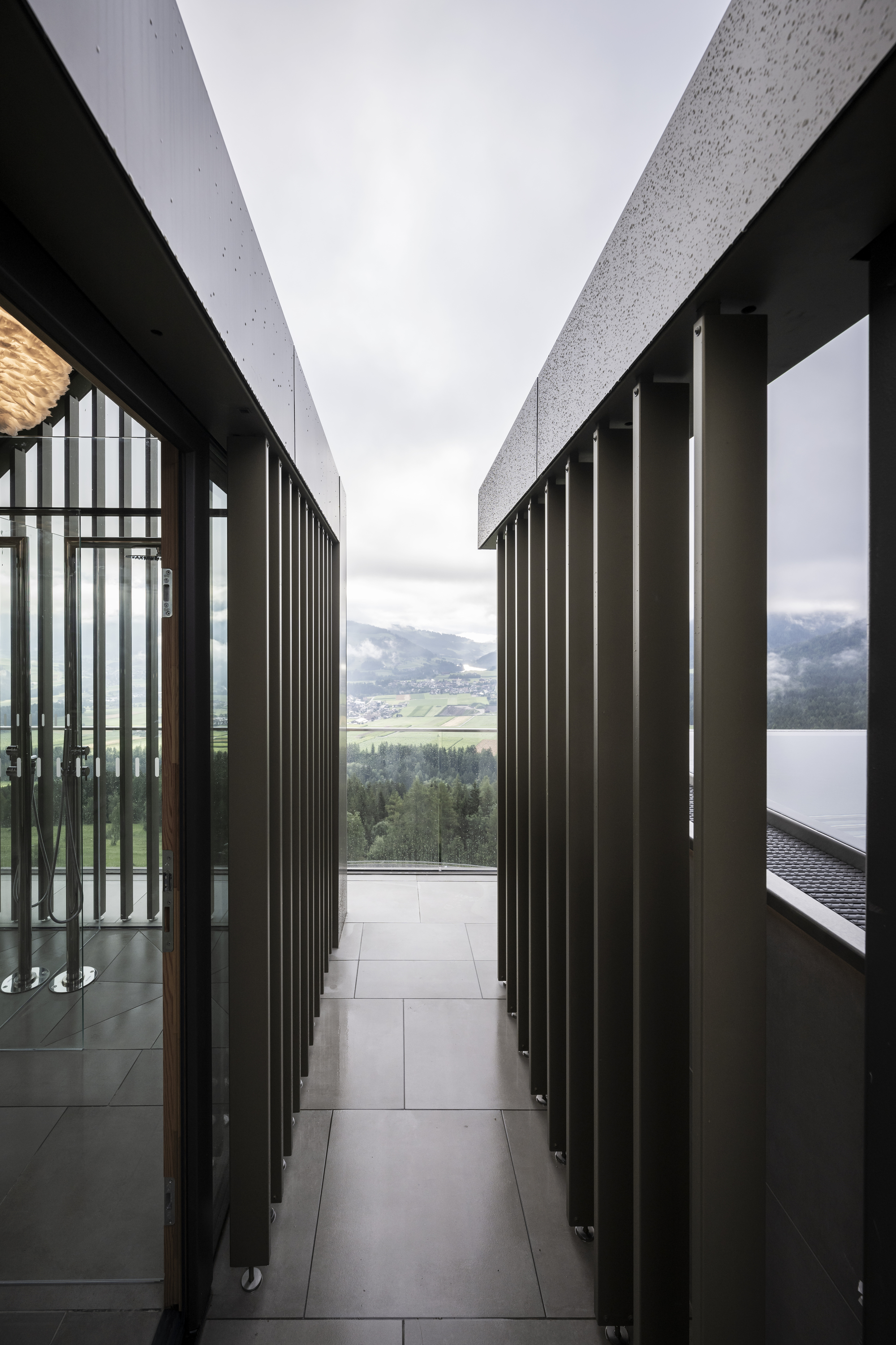 Narrow corridor with vertical metal screening opening to a lakeside mountain vista