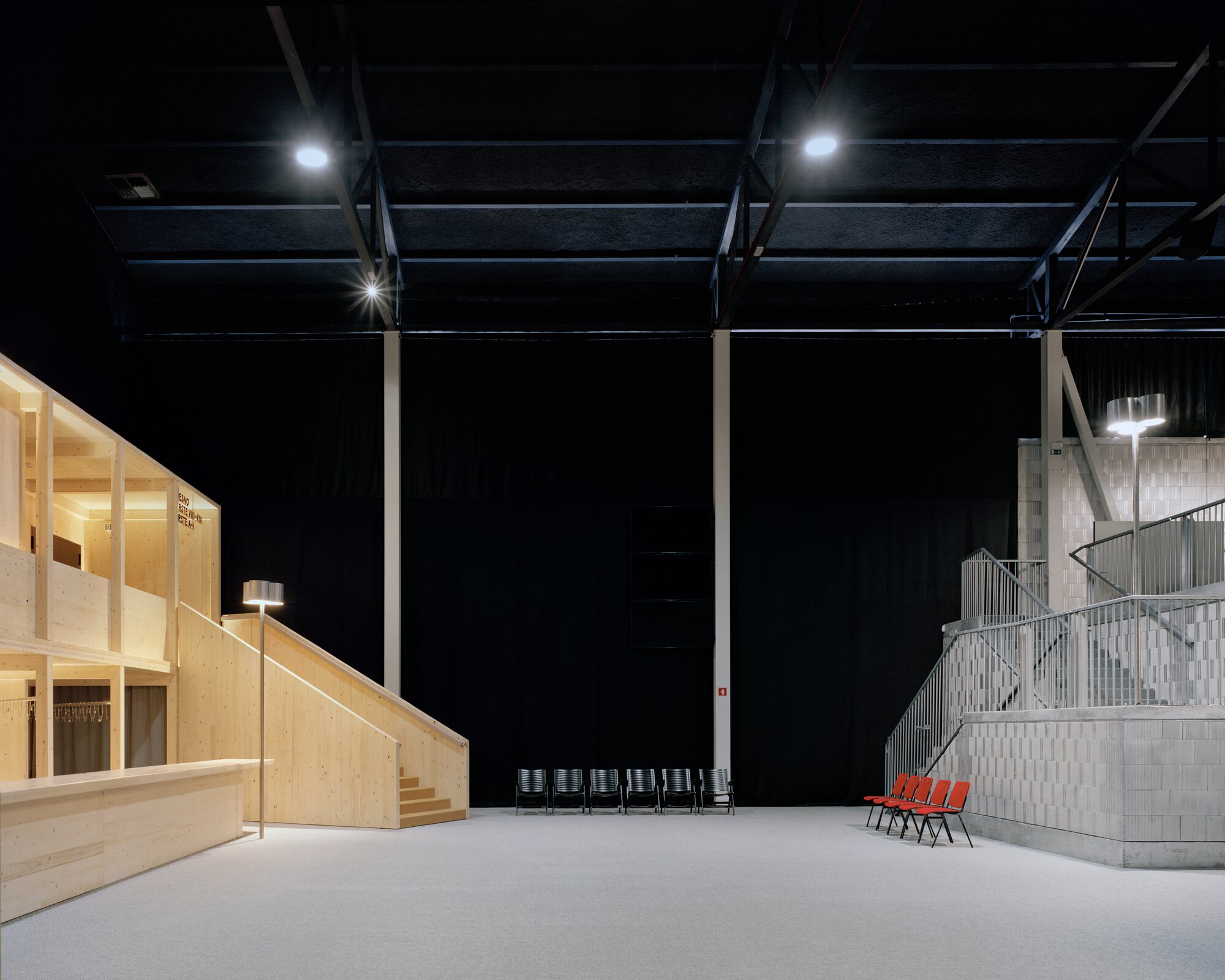 Plywood insert structure under the black-painted ceiling with red chairs and concrete stair beyond