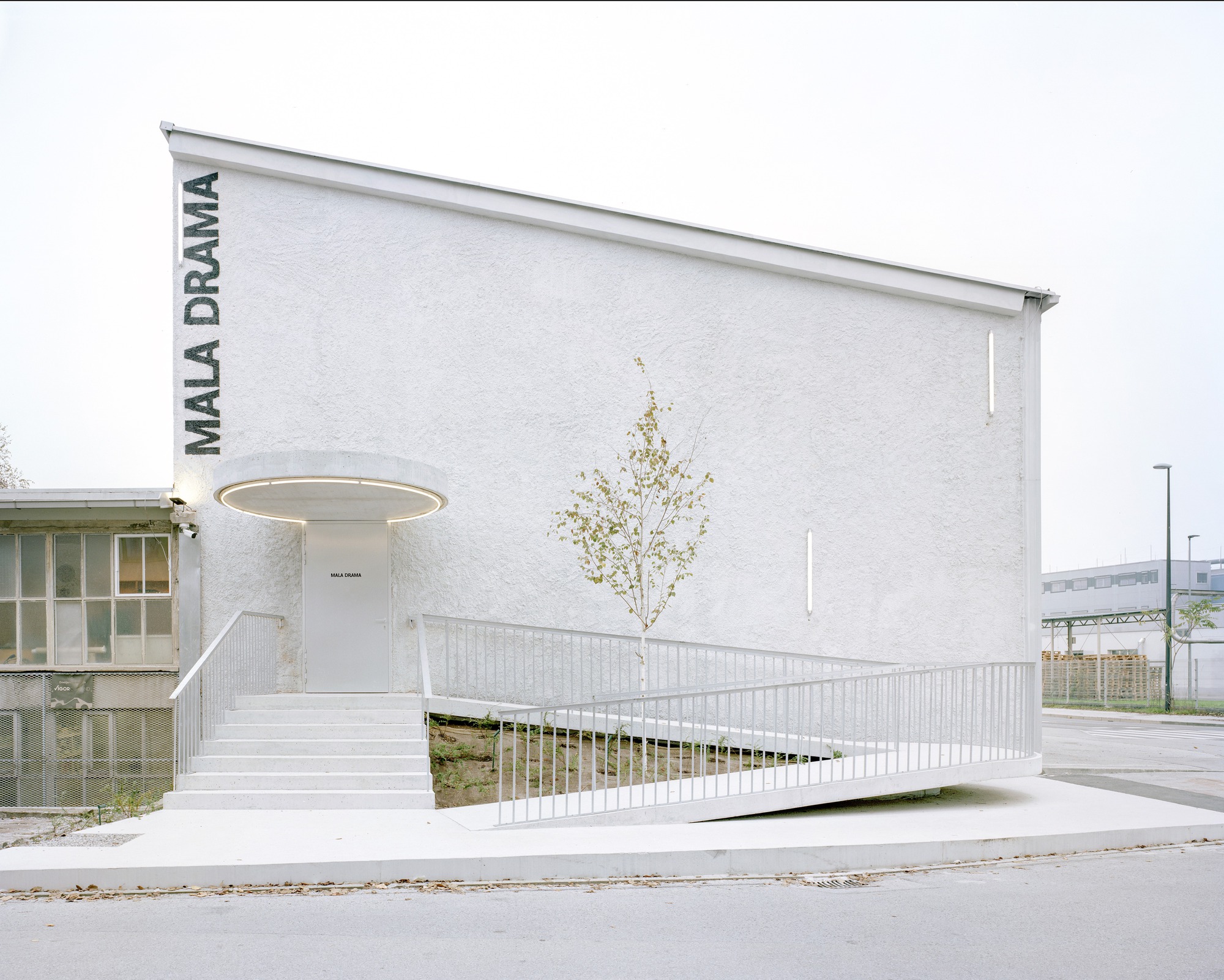 White stucco facade with ramped access and circular canopy at the entrance under overcast sky