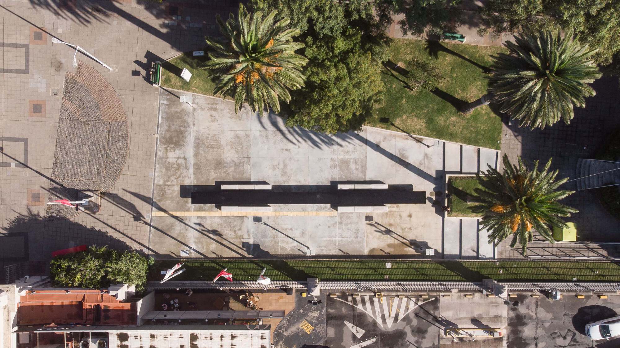Aerial view of a concrete plaza bordered by palm trees and a planted median strip