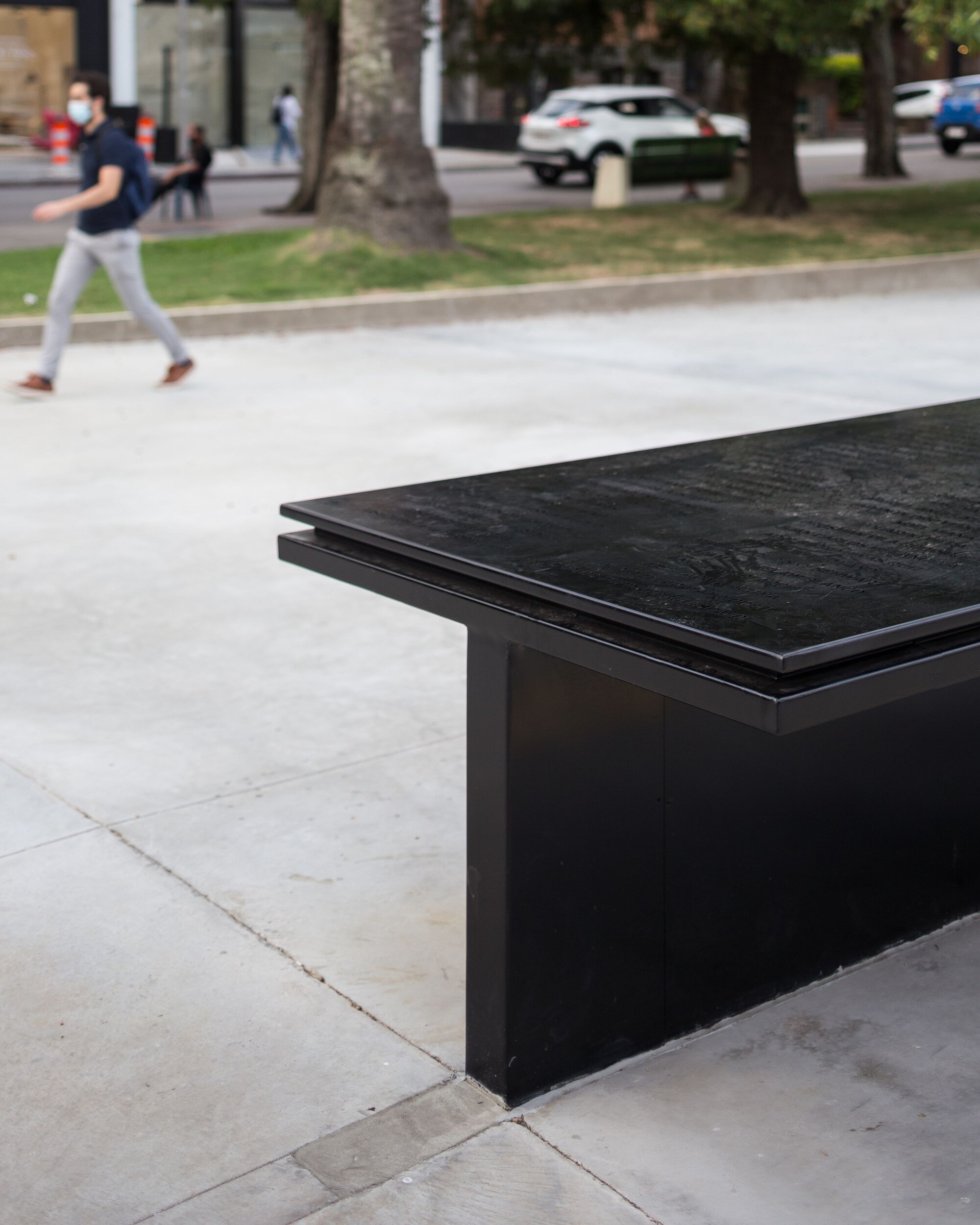 Black granite memorial bench with engraved surface in a public plaza with a pedestrian crossing