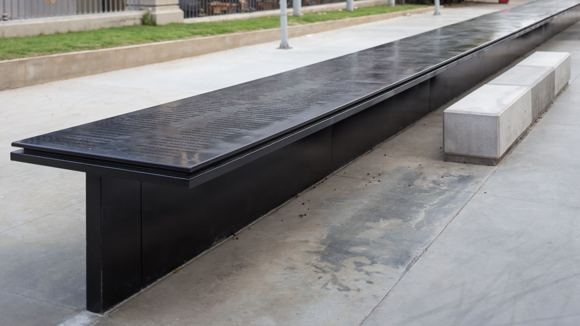 Extended view of the black granite memorial bench alongside white concrete block seating