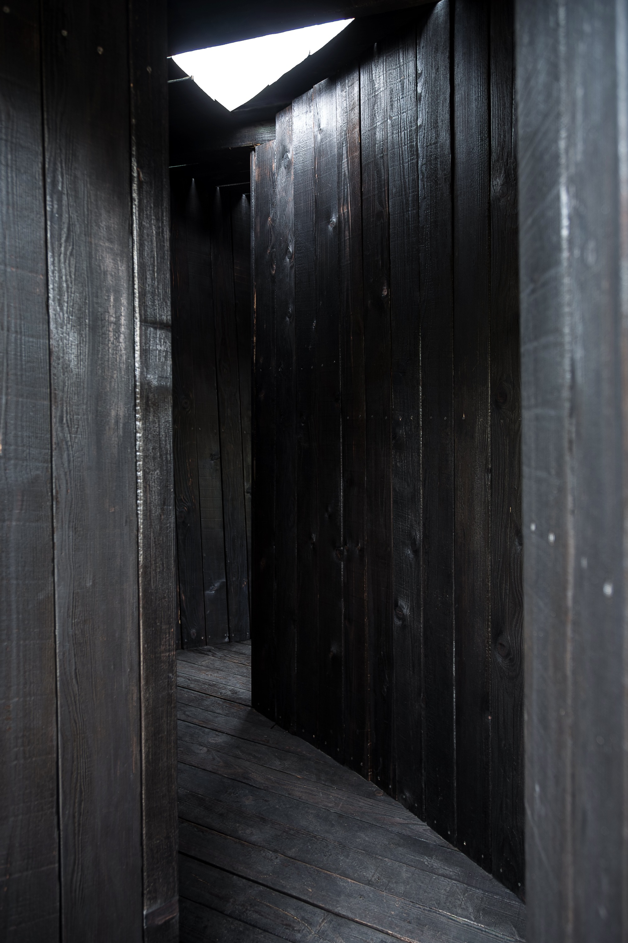 Dark timber interior corridor with triangular skylight casting bright daylight through the opening above