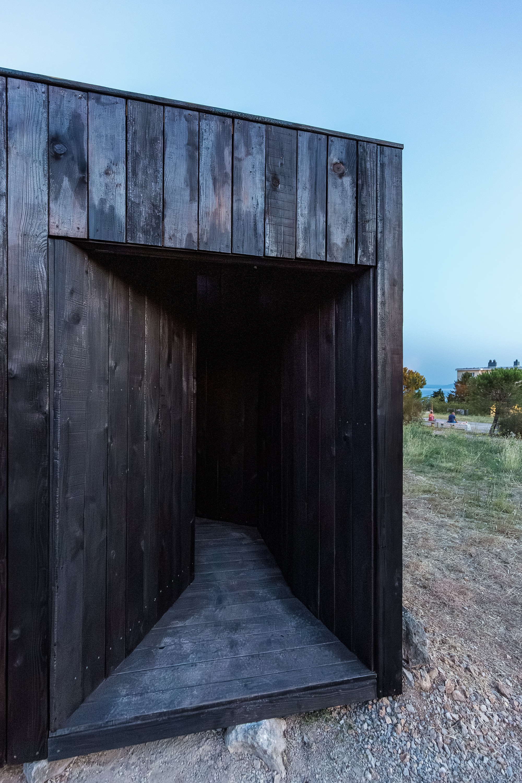 Recessed entrance through blackened timber walls leading to a dark interior corridor at dusk