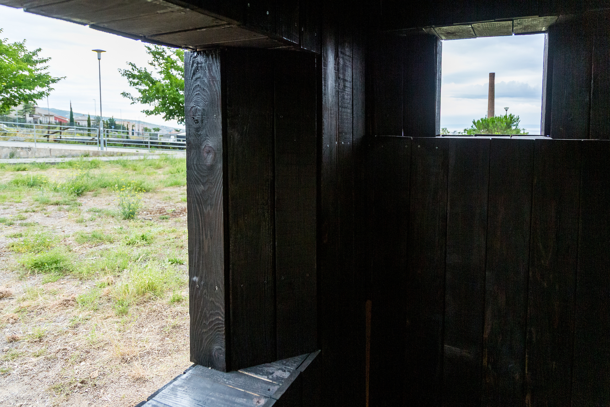Interior threshold space with charred timber walls framing horizontal window openings to the landscape