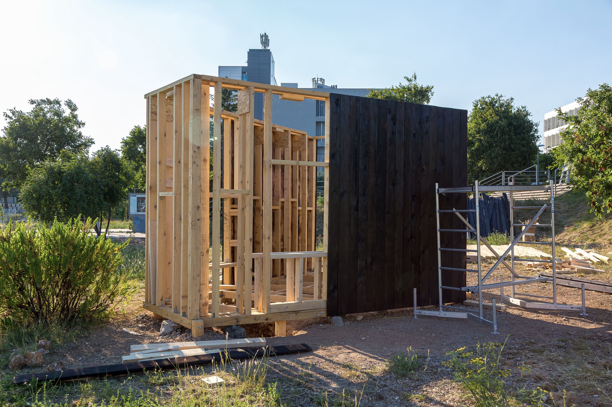 Partially enclosed pavilion showing light timber framing alongside charred vertical wood siding in afternoon sun