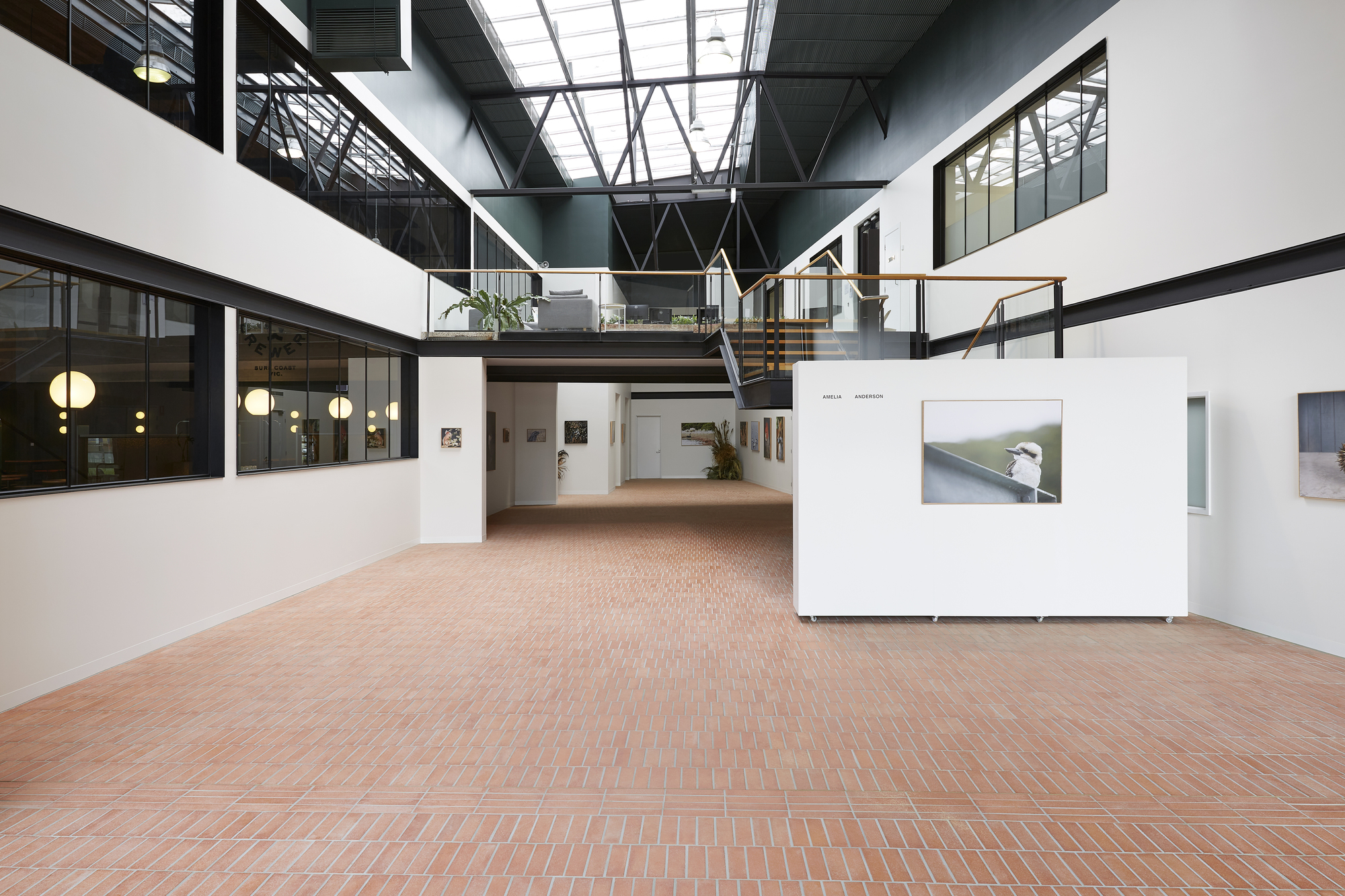 Double-height atrium with mezzanine walkway, skylights and freestanding white exhibition panels on herringbone brick floor