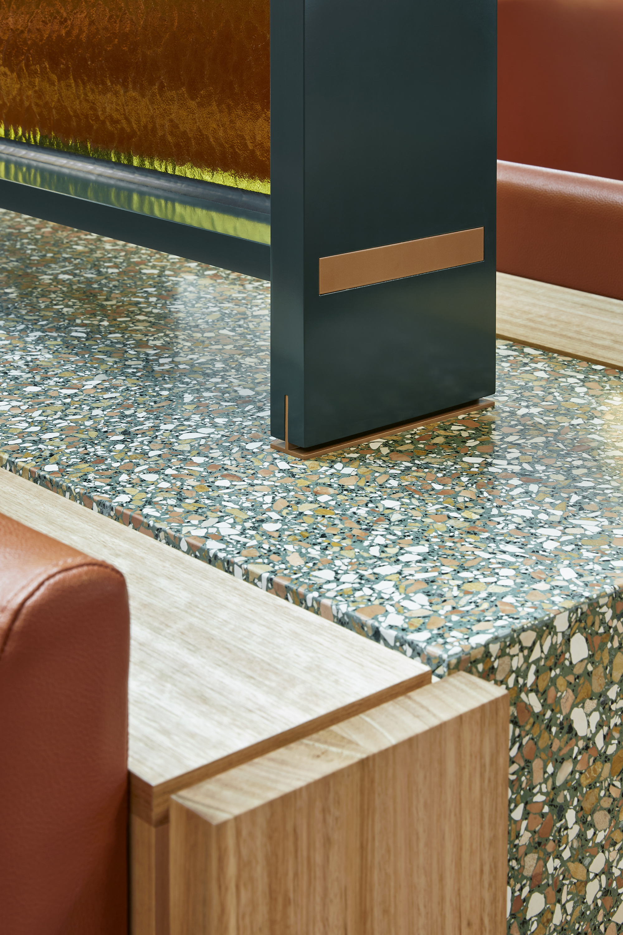 Detail of terrazzo countertop meeting dark painted column with bronze metal accent strip