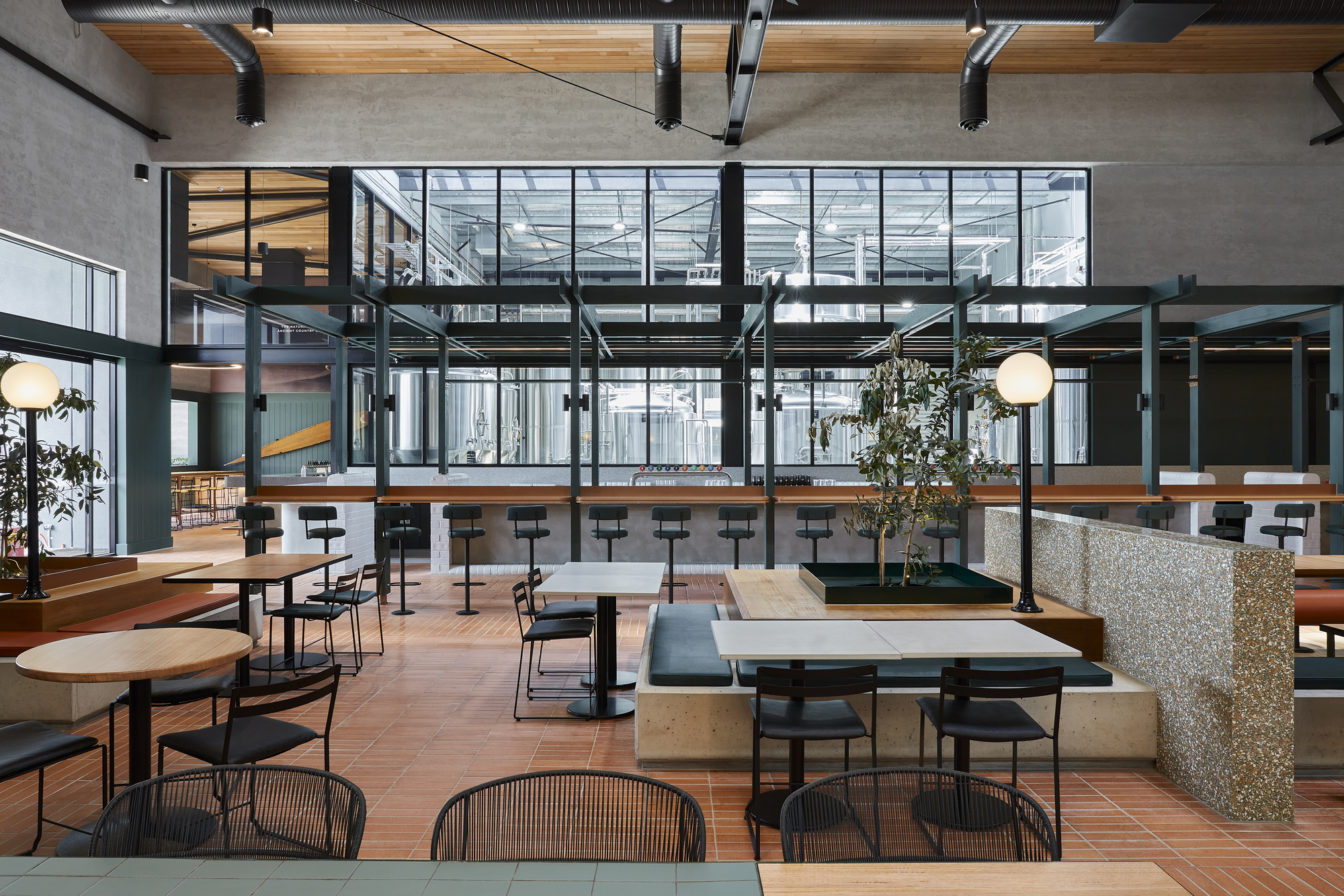 Double-height dining space with steel frame mezzanine, timber ceiling, and terrazzo column bases