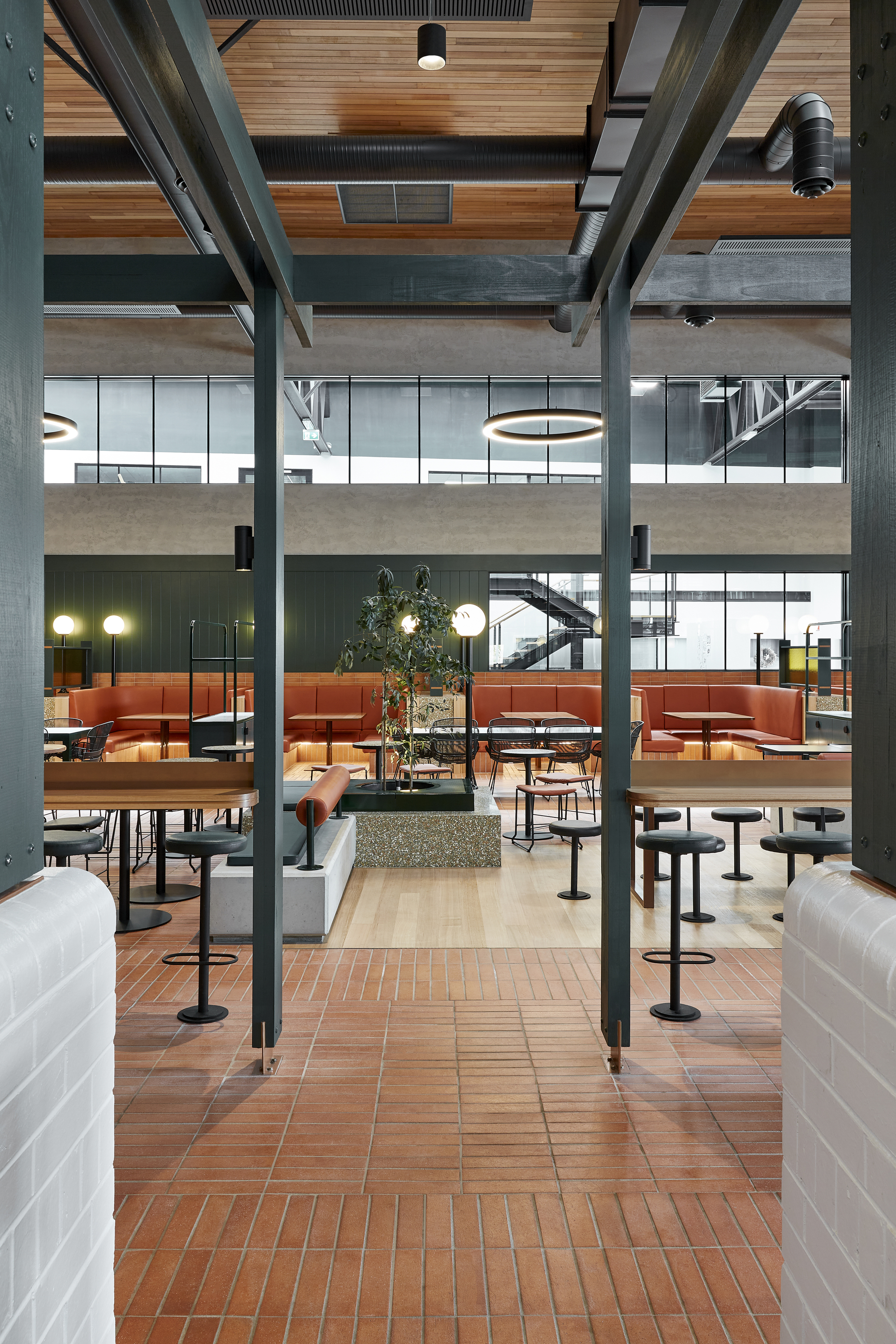 View through the double-height interior showing steel structure, timber ceiling slats, and seated dining areas