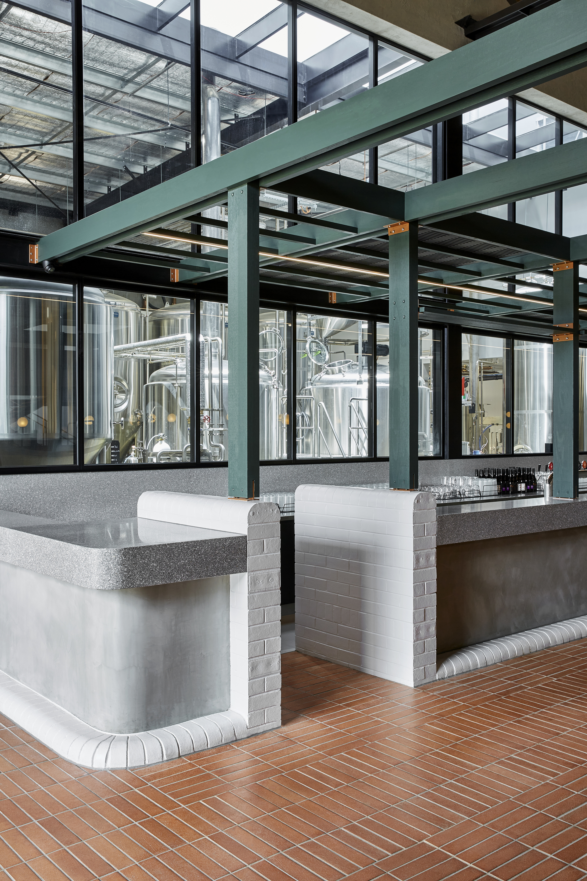 Banquette seating with terrazzo counters and white tiled bases beneath steel mezzanine structure