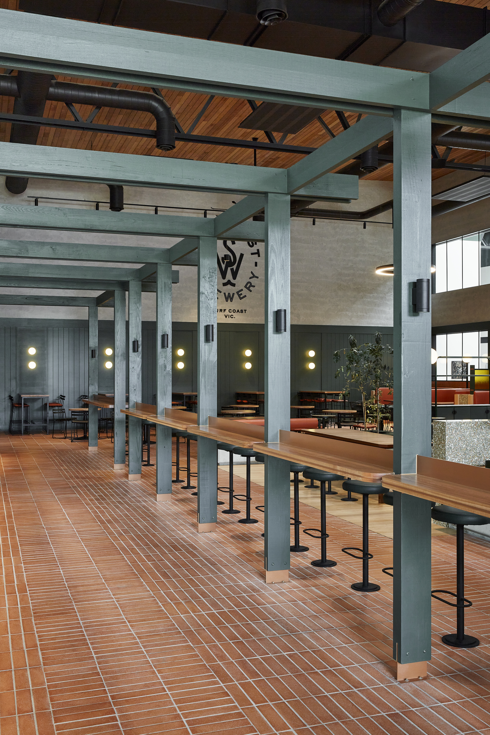 Long communal tables with steel columns and timber ceiling under blue painted beams