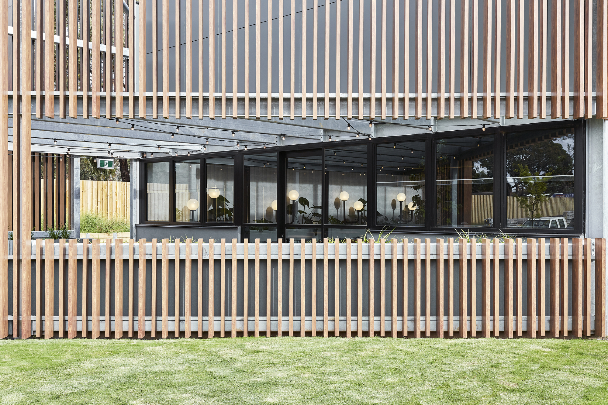 Exterior facade with vertical timber screen wrapping glass windows above a manicured lawn