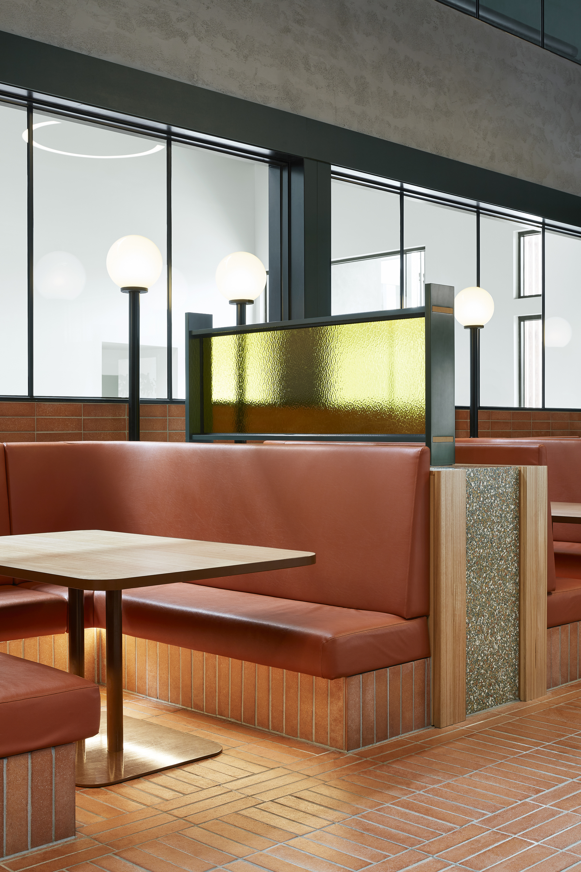 Booth seating with terracotta tile base and teal upholstery below a backlit brass panel and globe fixtures