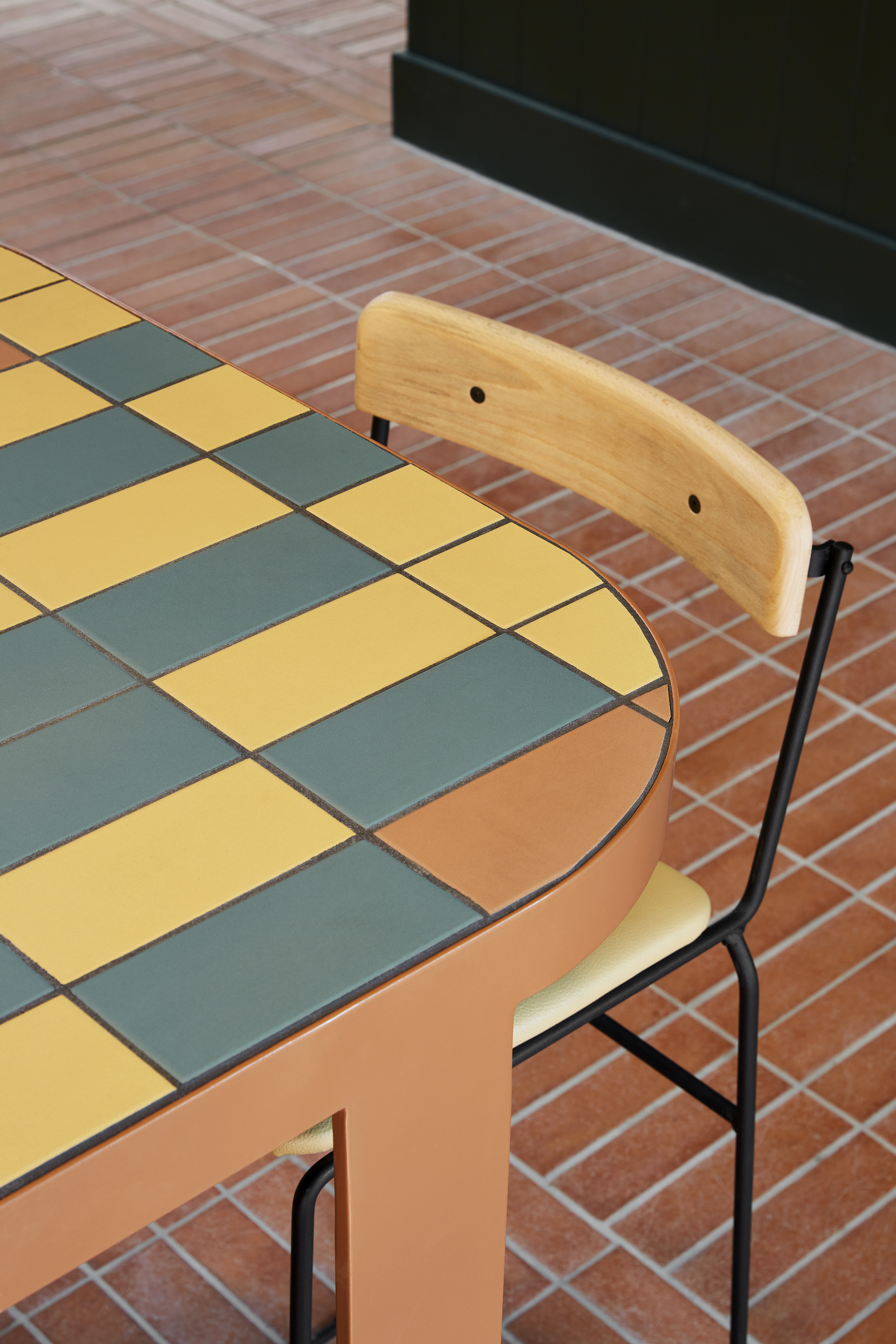 Tabletop with yellow and grey checkered tiles beside a wooden chair on herringbone brick flooring