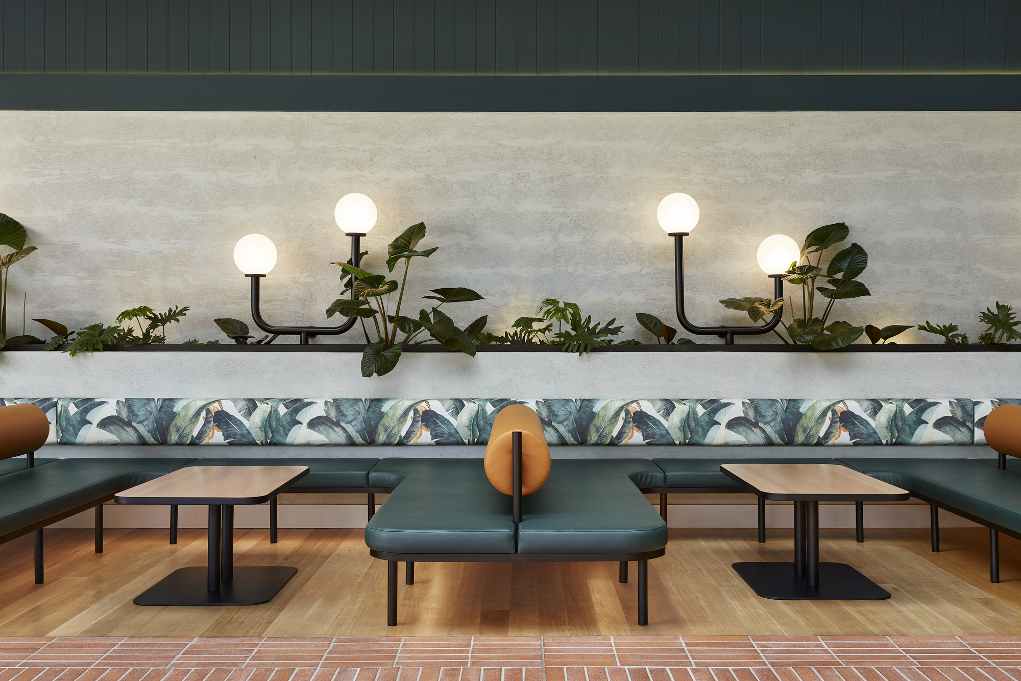 Symmetrical view of booth seating with botanical upholstery and planted ledge illuminated by globe sconces