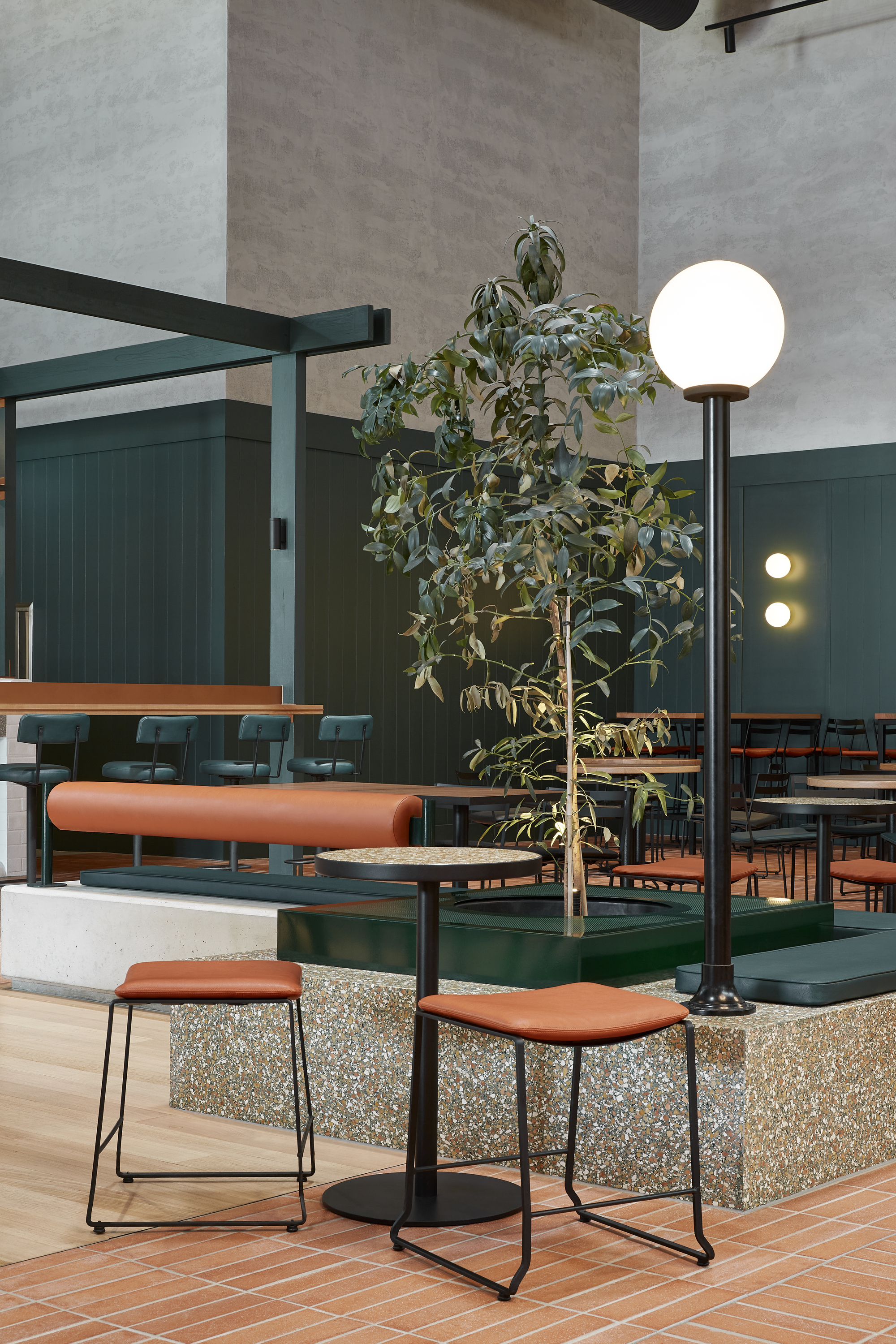 Raised terrazzo platform with bar stools and potted tree beneath a globe floor lamp