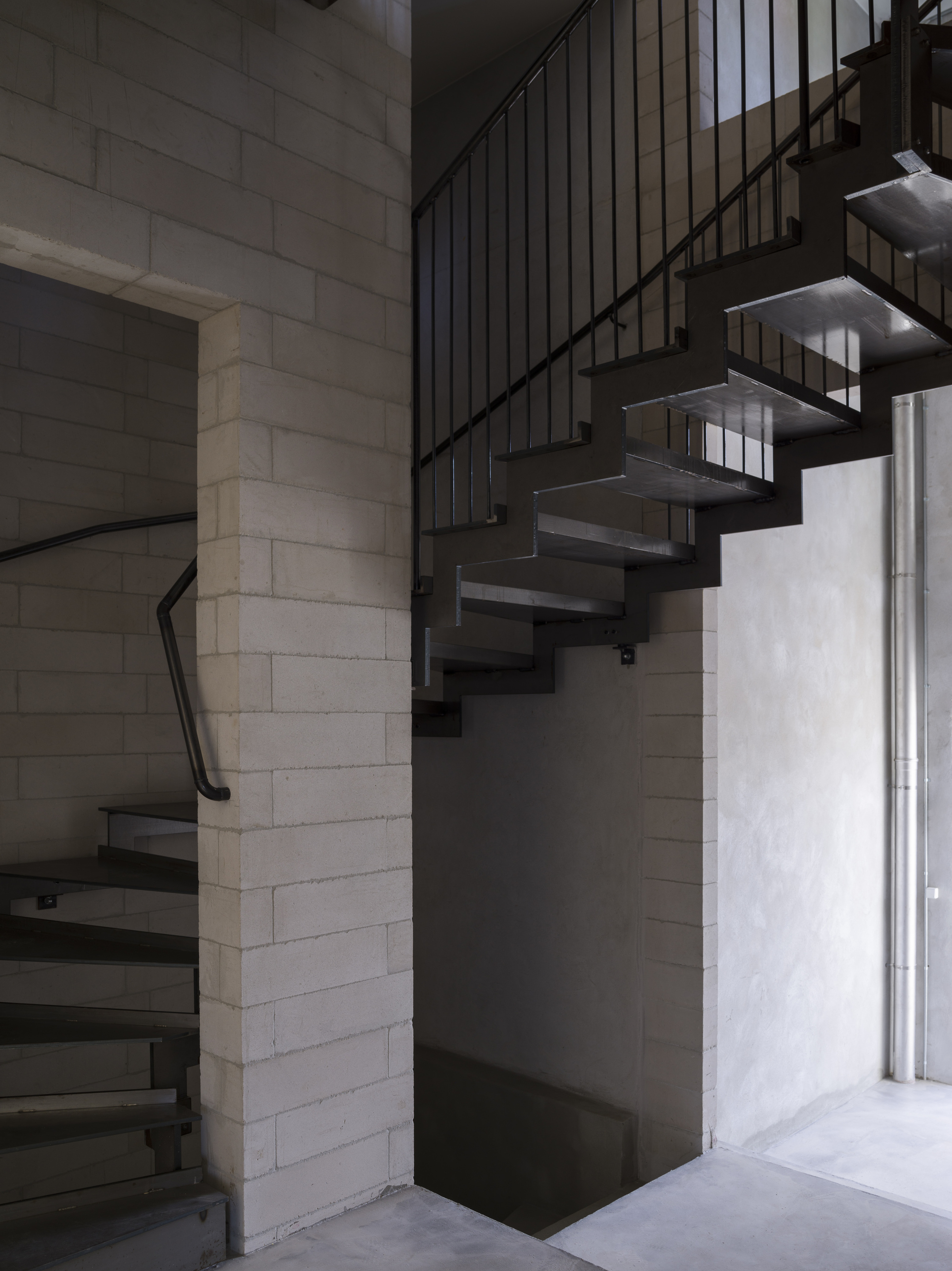 Steel open-tread staircase winding between concrete block walls with vertical metal railing