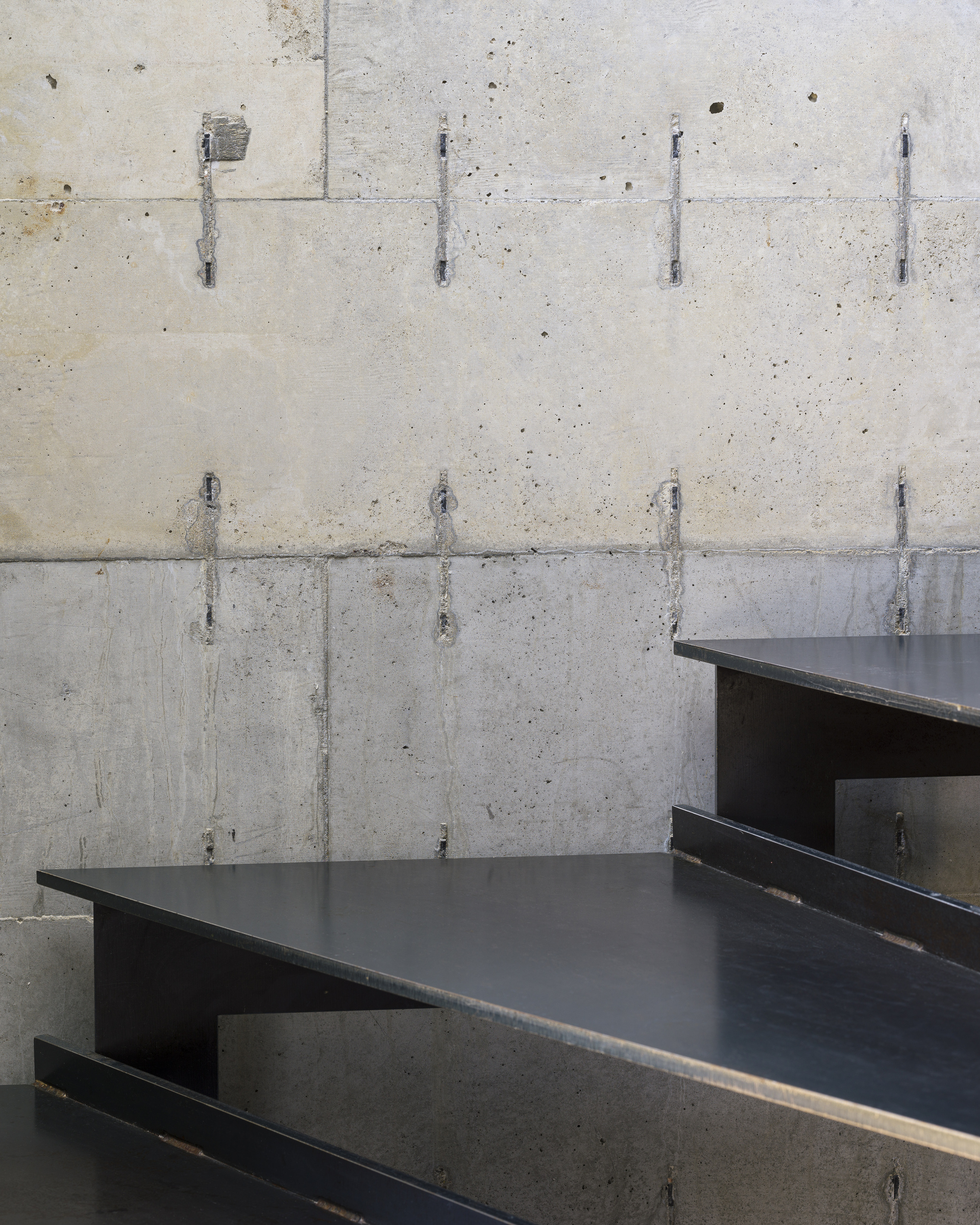Close-up of steel stair treads cantilevered from board-formed concrete wall with tie holes