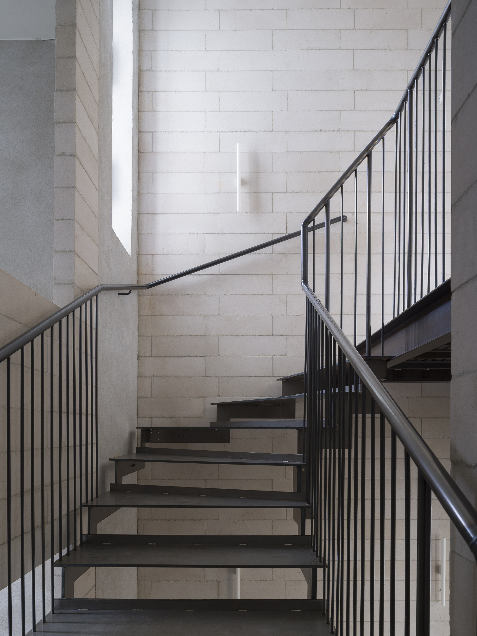 Steel staircase with vertical bar railings ascending between white concrete block walls