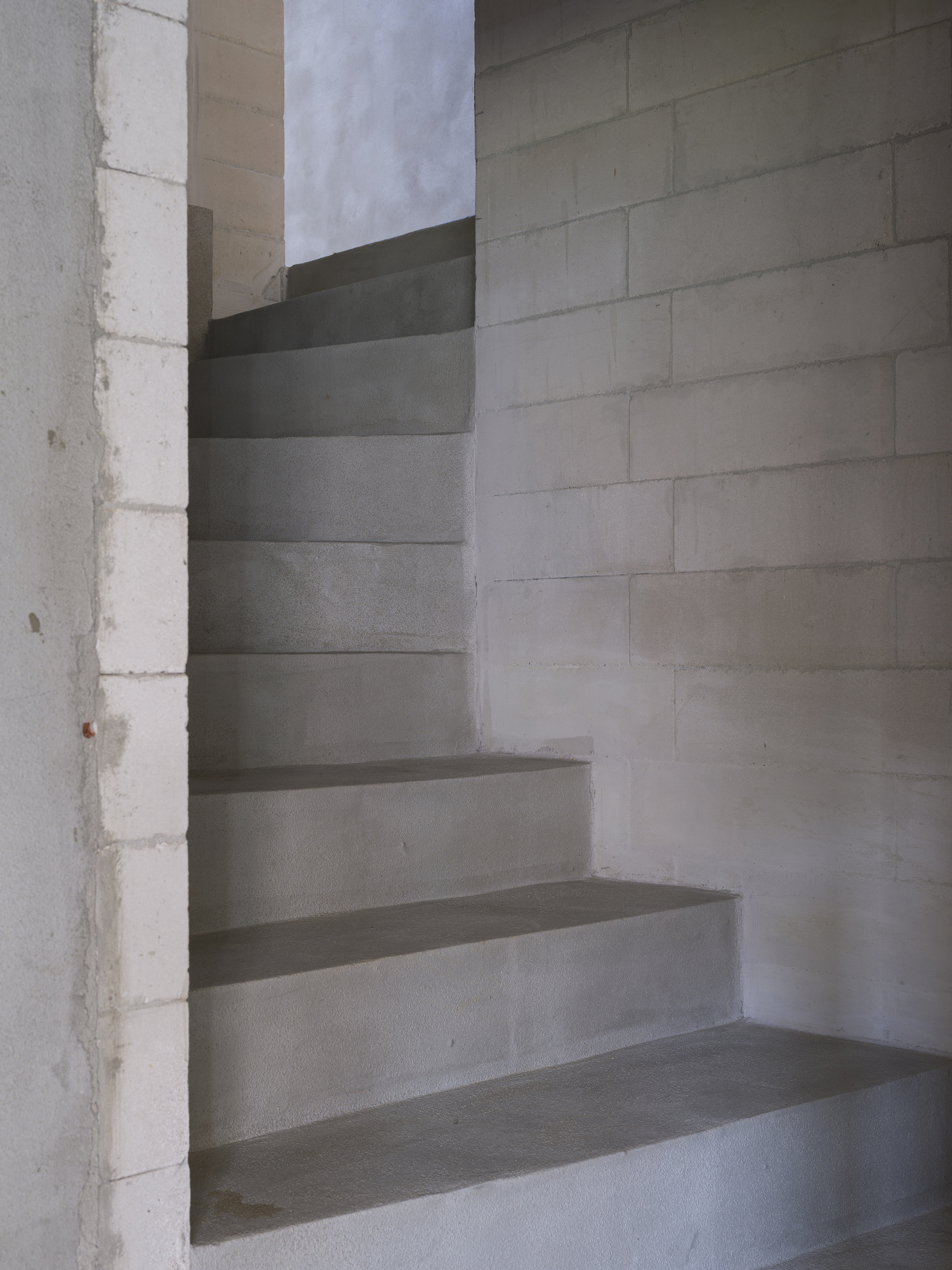 Concrete spiral staircase winding upward through a cylindrical shaft open to cloudy sky