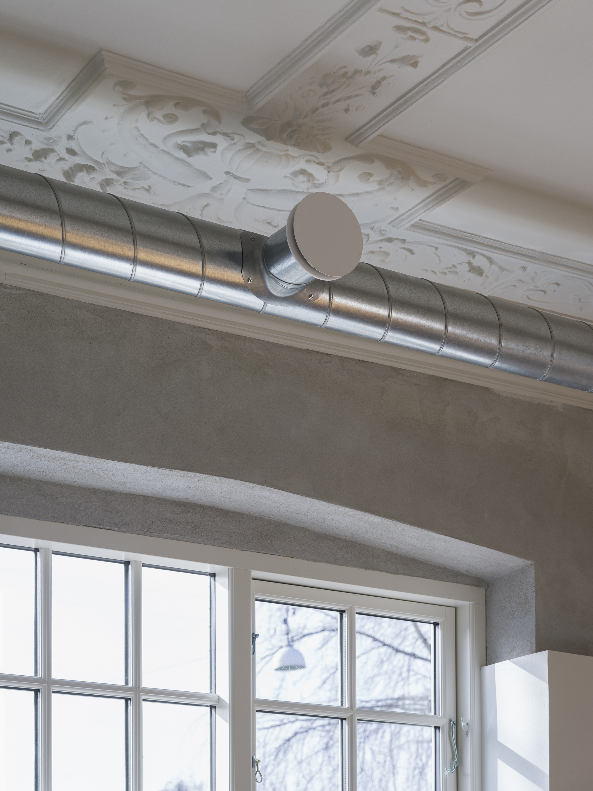 Exposed spiral ductwork running below decorative white ceiling molding near gridded windows
