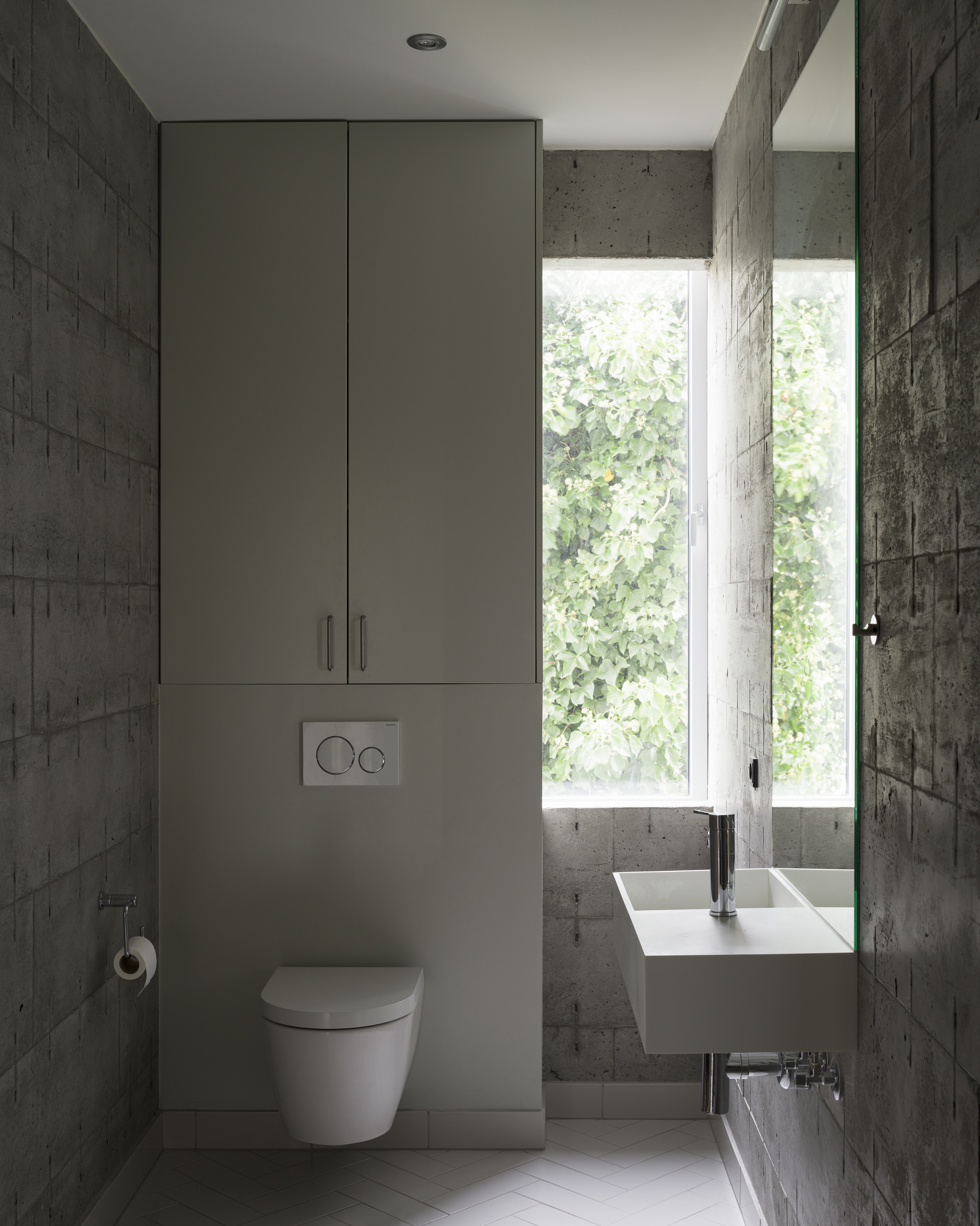 Bathroom with wall-hung basin, tall storage cabinet, and window overlooking green foliage outside