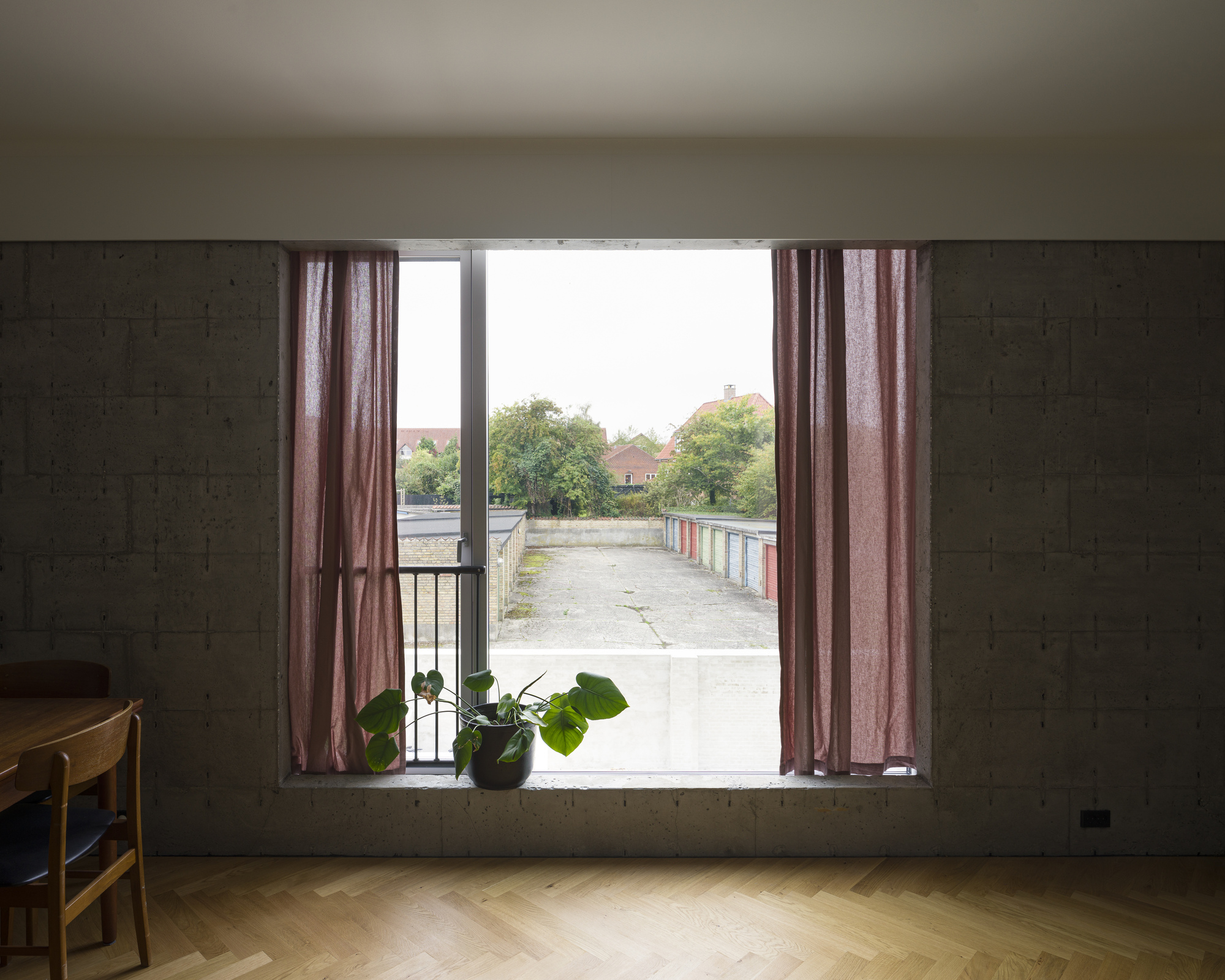 Wide window with pink curtains framing a view of a concrete terrace and distant trees