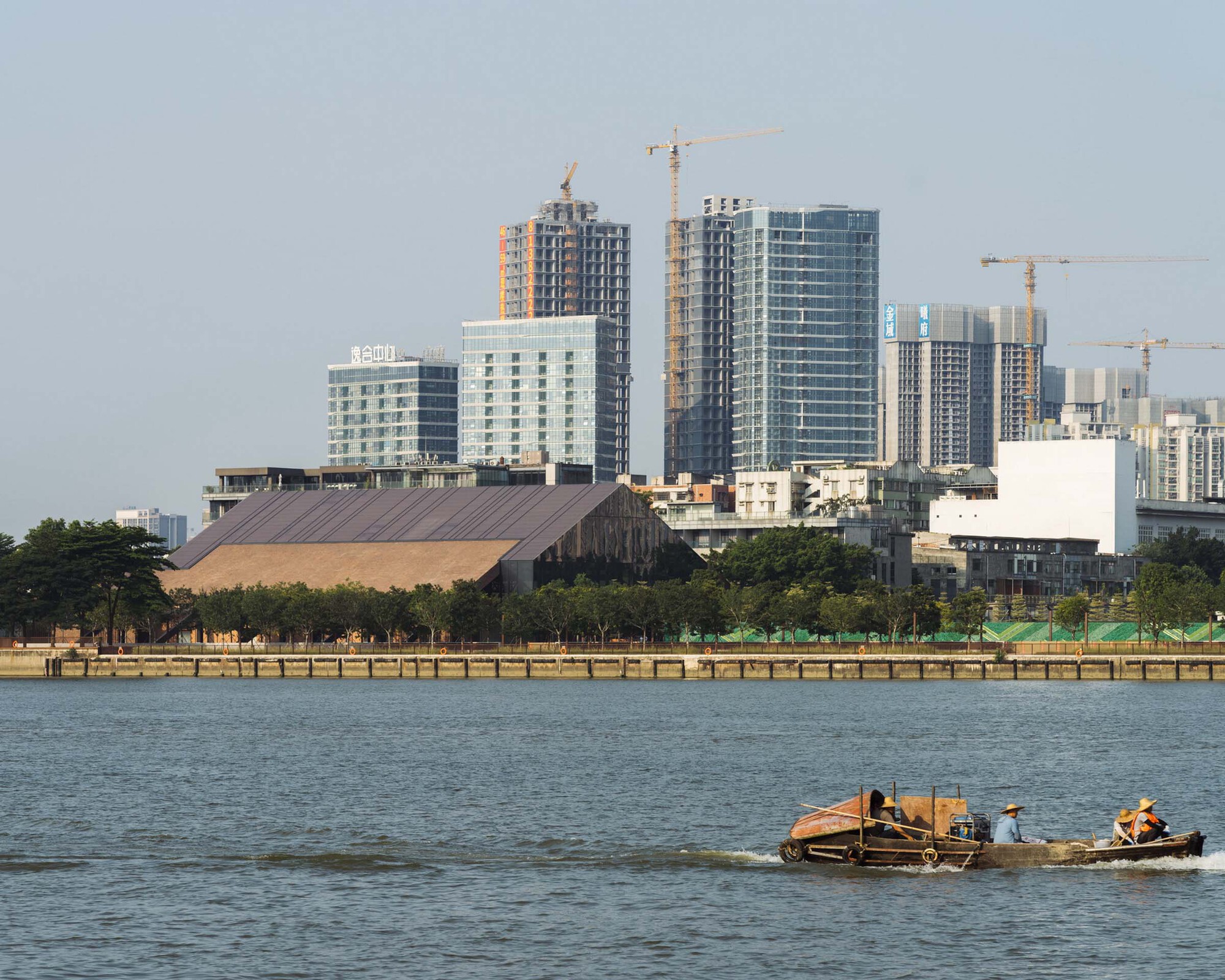 Waterfront view of the timber-clad roof structure against highrise towers under construction