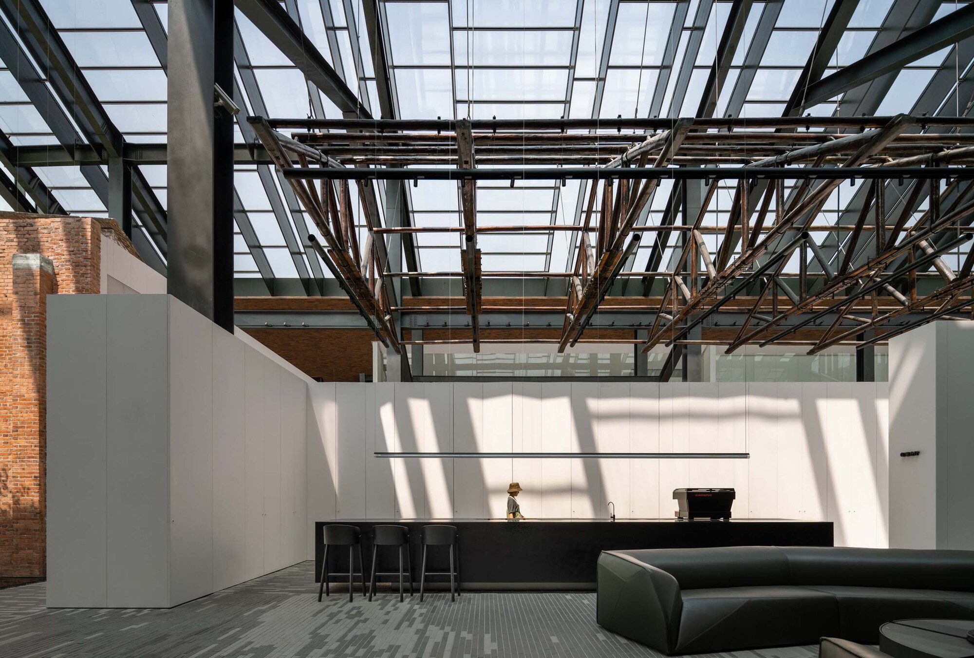 Interior space with exposed steel truss ceiling and glazed roof casting geometric shadows across white walls