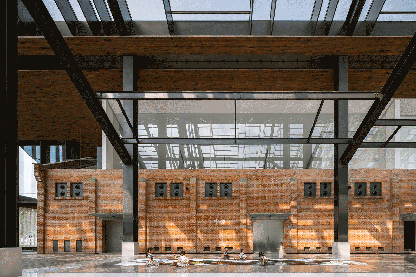 Interior view of retained brick wall with steel openings under a glass and steel trussed roof