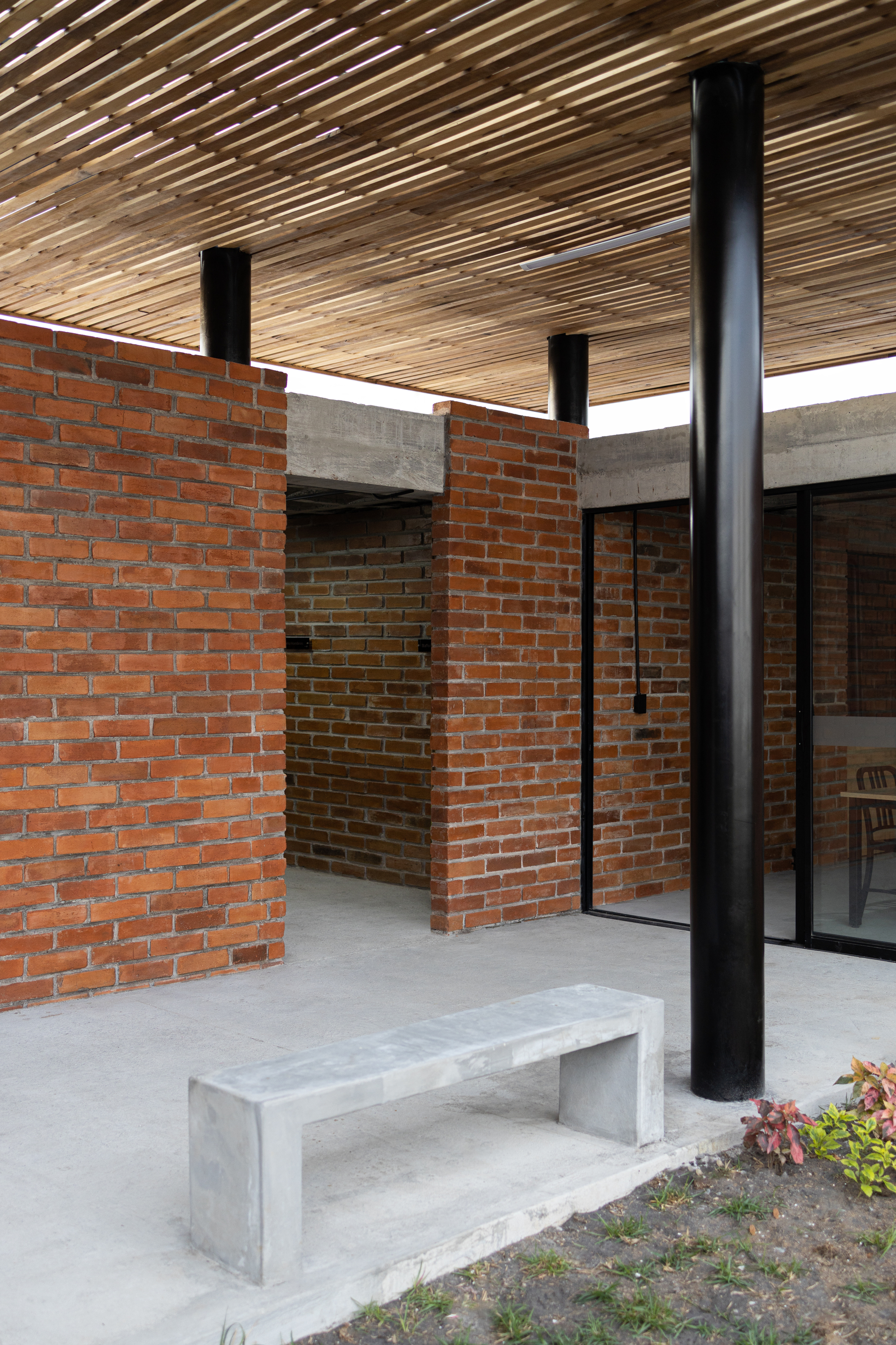 Courtyard space with red brick walls, concrete lintel, and timber slat canopy supported by black columns