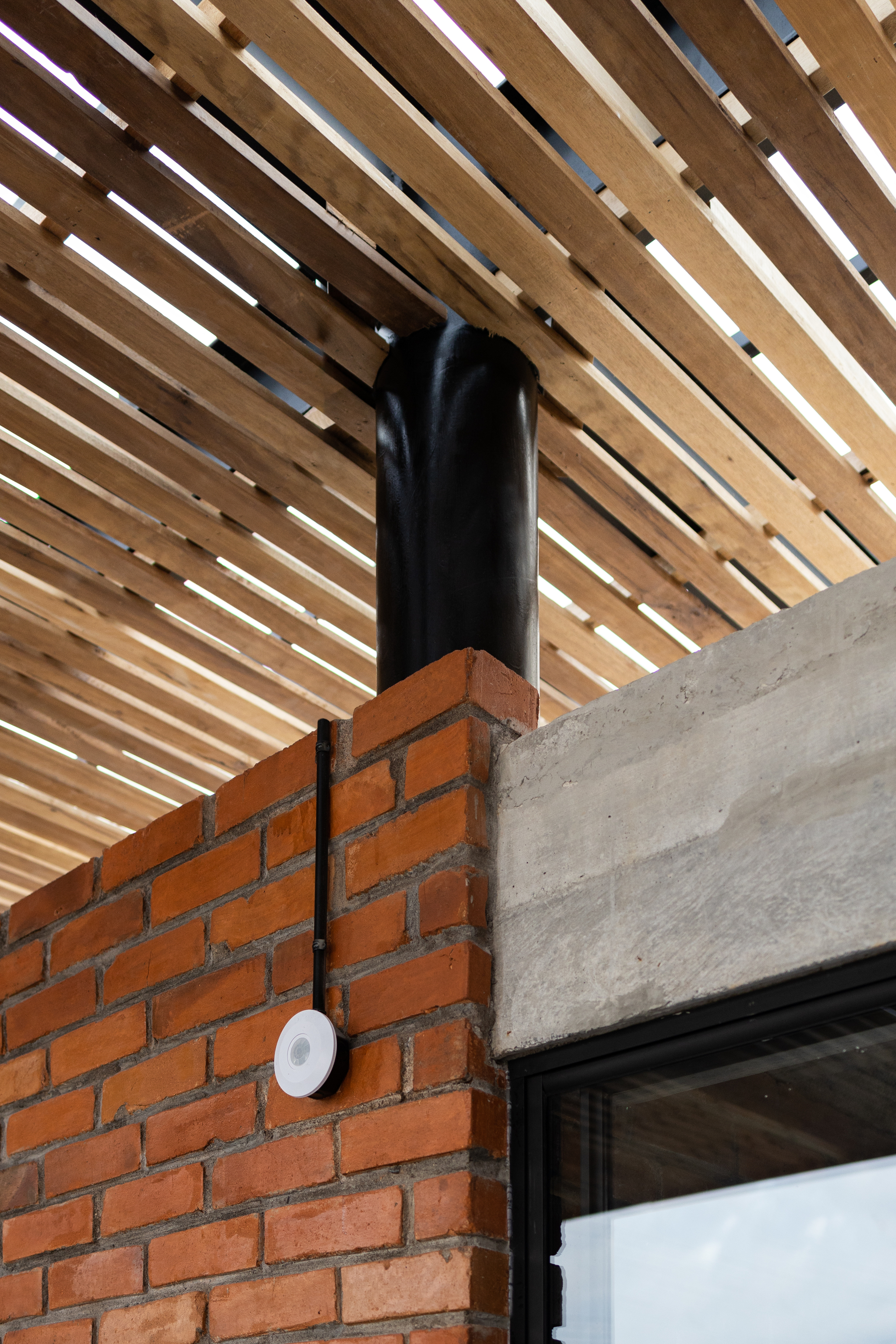 Detail of black steel column meeting red brick wall and concrete beam beneath slatted timber soffit