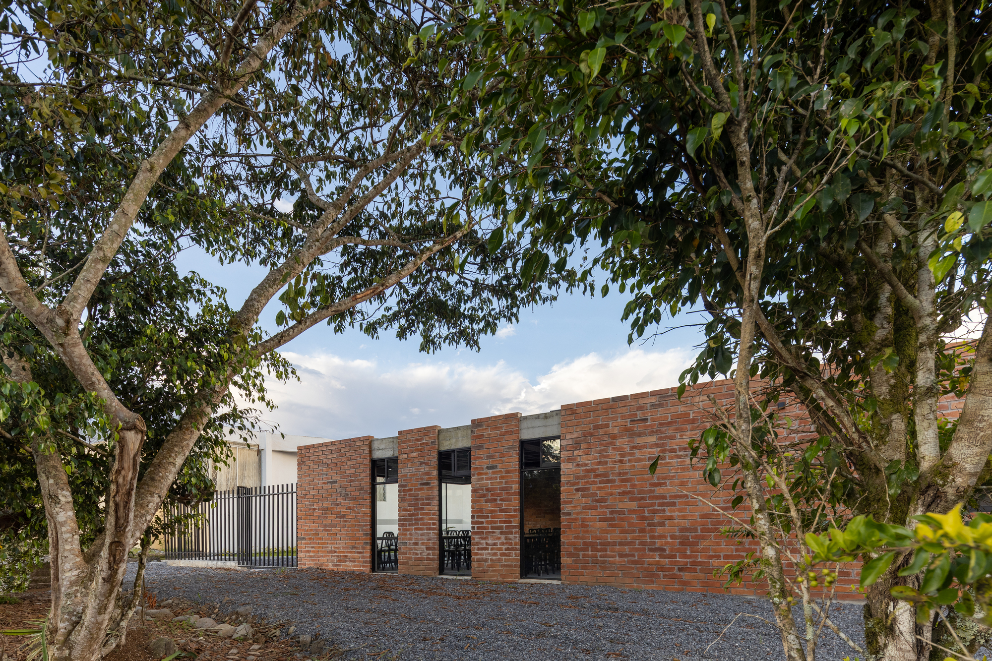 Red brick facade with vertical slit windows seen through mature trees in the late afternoon