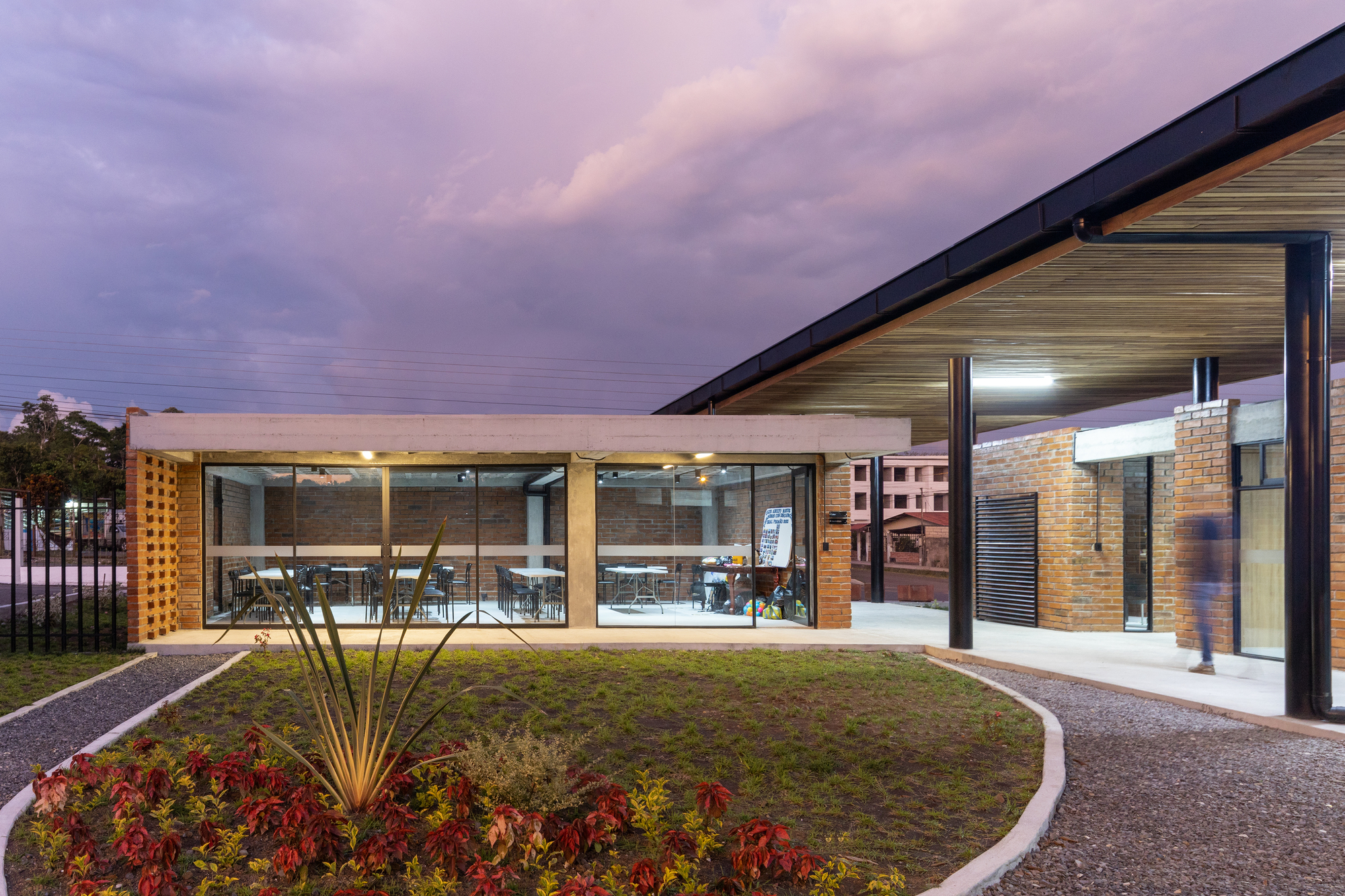 Green roof courtyard with glass-walled dining area and landscape lighting under a purple twilight sky