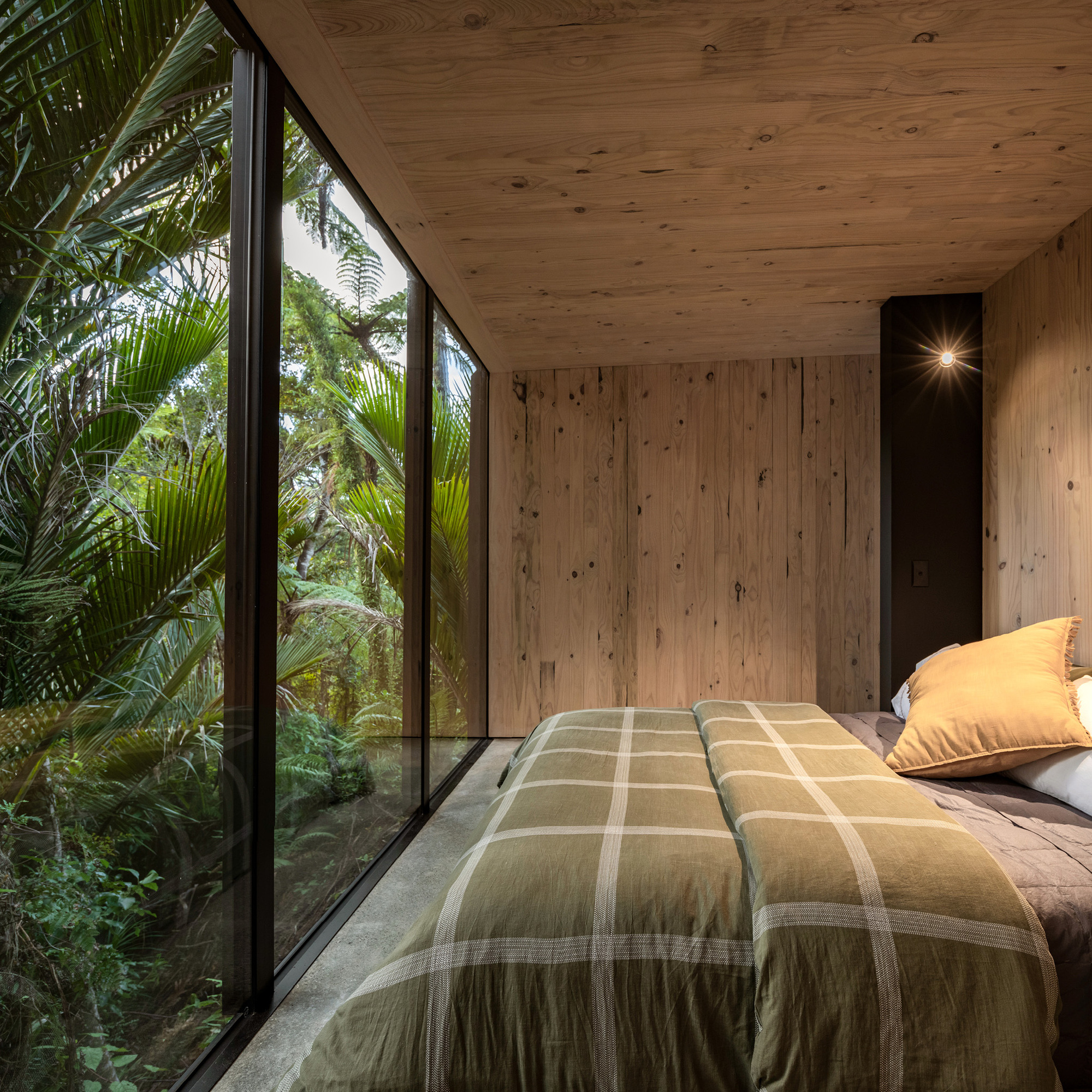 Sleeping area with plywood walls and ceiling and angled glazing overlooking palm fronds