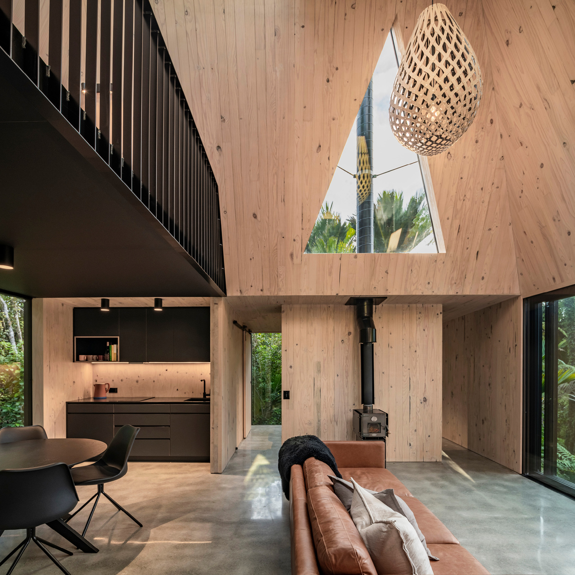 Double-height living space with vertical timber lining, triangular skylight and woven pendant light above polished concrete floor