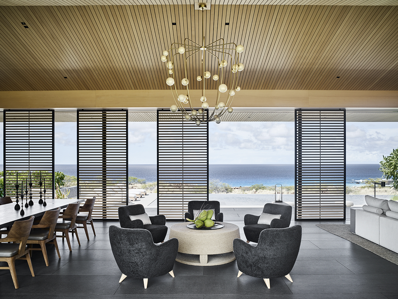 Open plan living space with horizontal louvered screens framing ocean horizon and pendant chandelier
