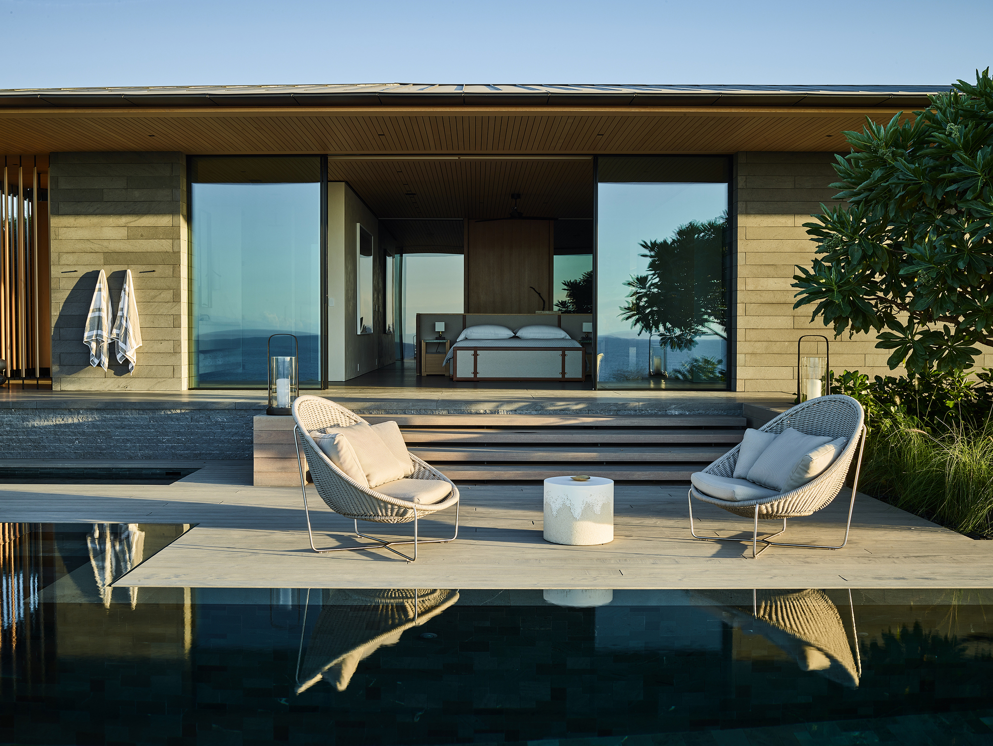 Poolside terrace with timber decking and slatted ceiling opening to a bedroom with ocean views