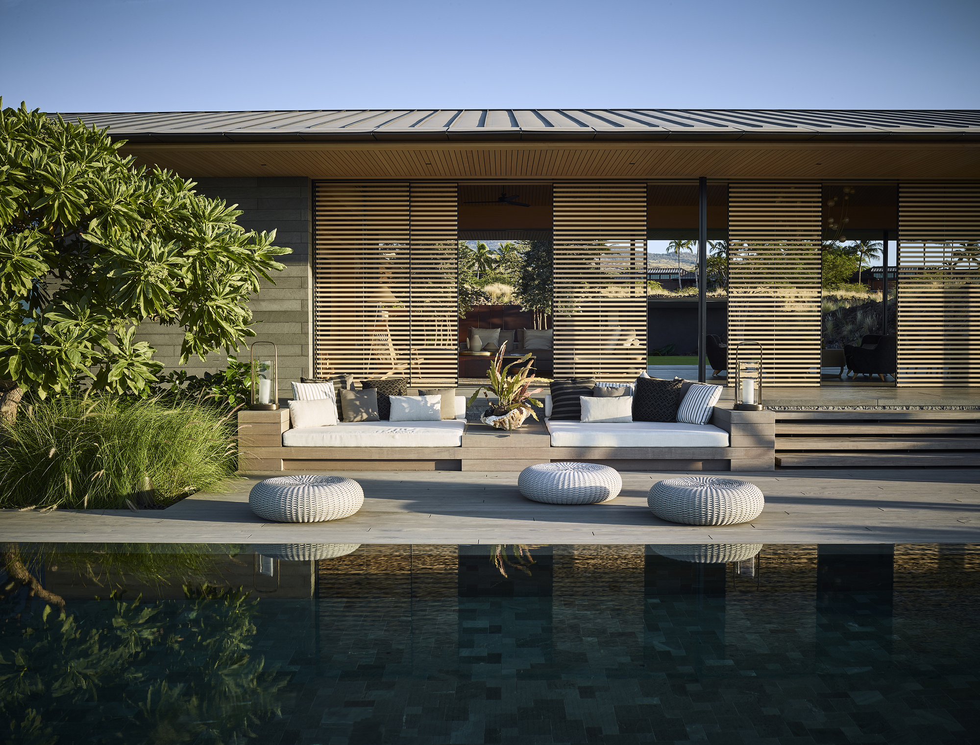 Horizontal timber louvers screening the glazed facade above a reflecting pool and terrace seating