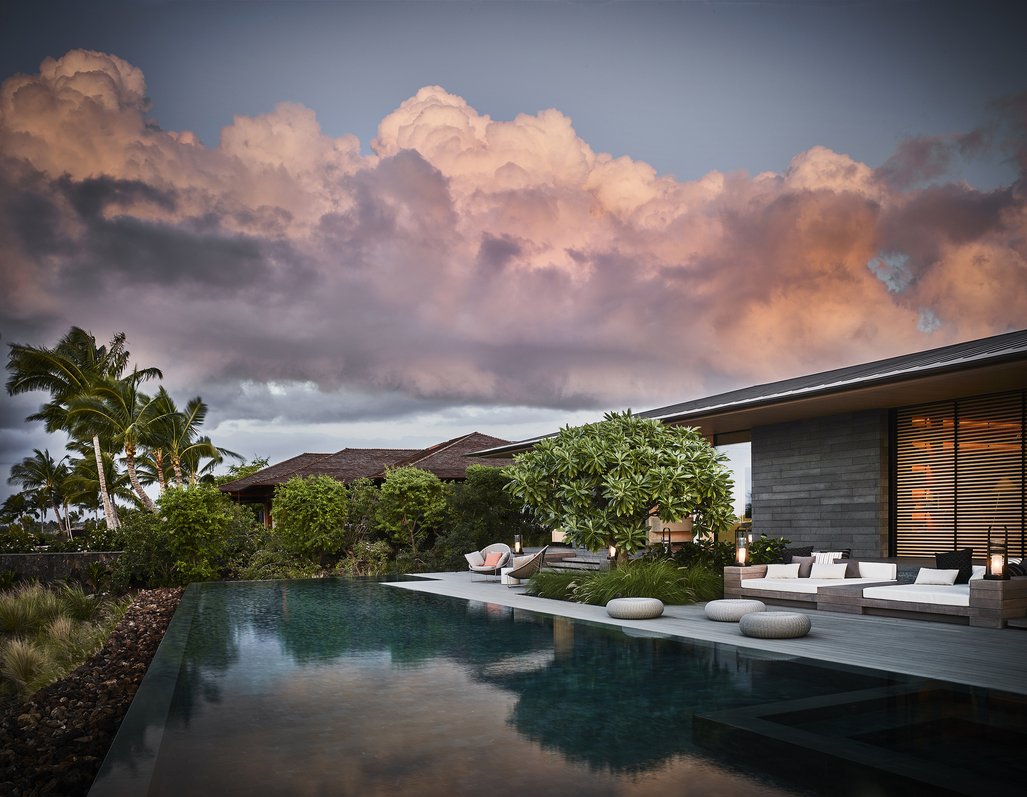 Pool terrace with horizontal louvers and planted beds beneath a dramatic storm cloud formation at dusk